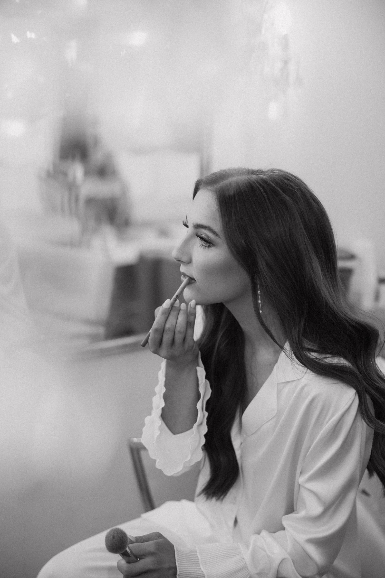 A woman in a white robe sits in profile during a beauty preparation session in black and white photography.