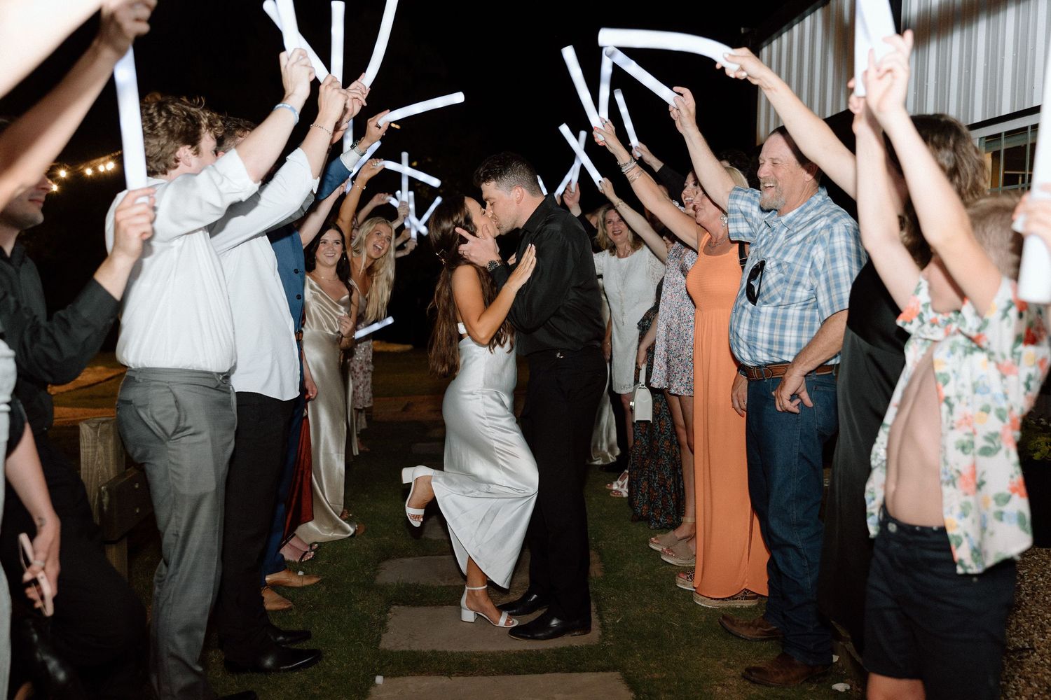 Wedding guests dance with raised arms on a wooden dance floor at an indoor reception celebration.