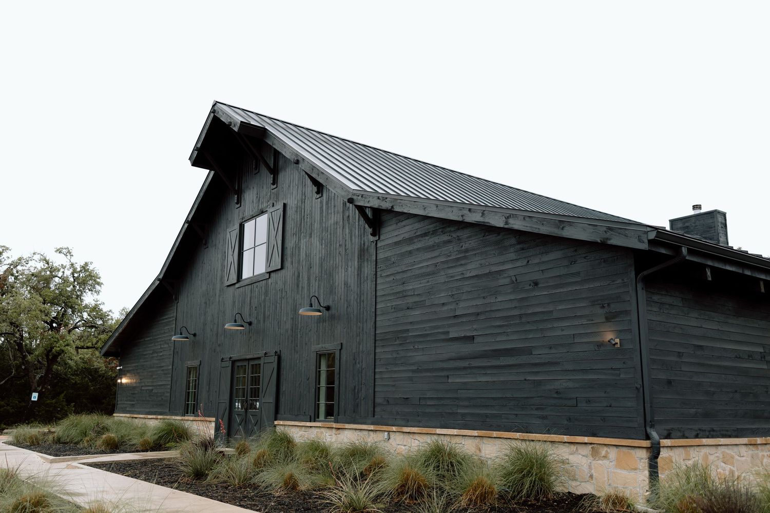 Dark green wooden barn with weathered siding and sloped roof stands against cloudy sky in rural setting.