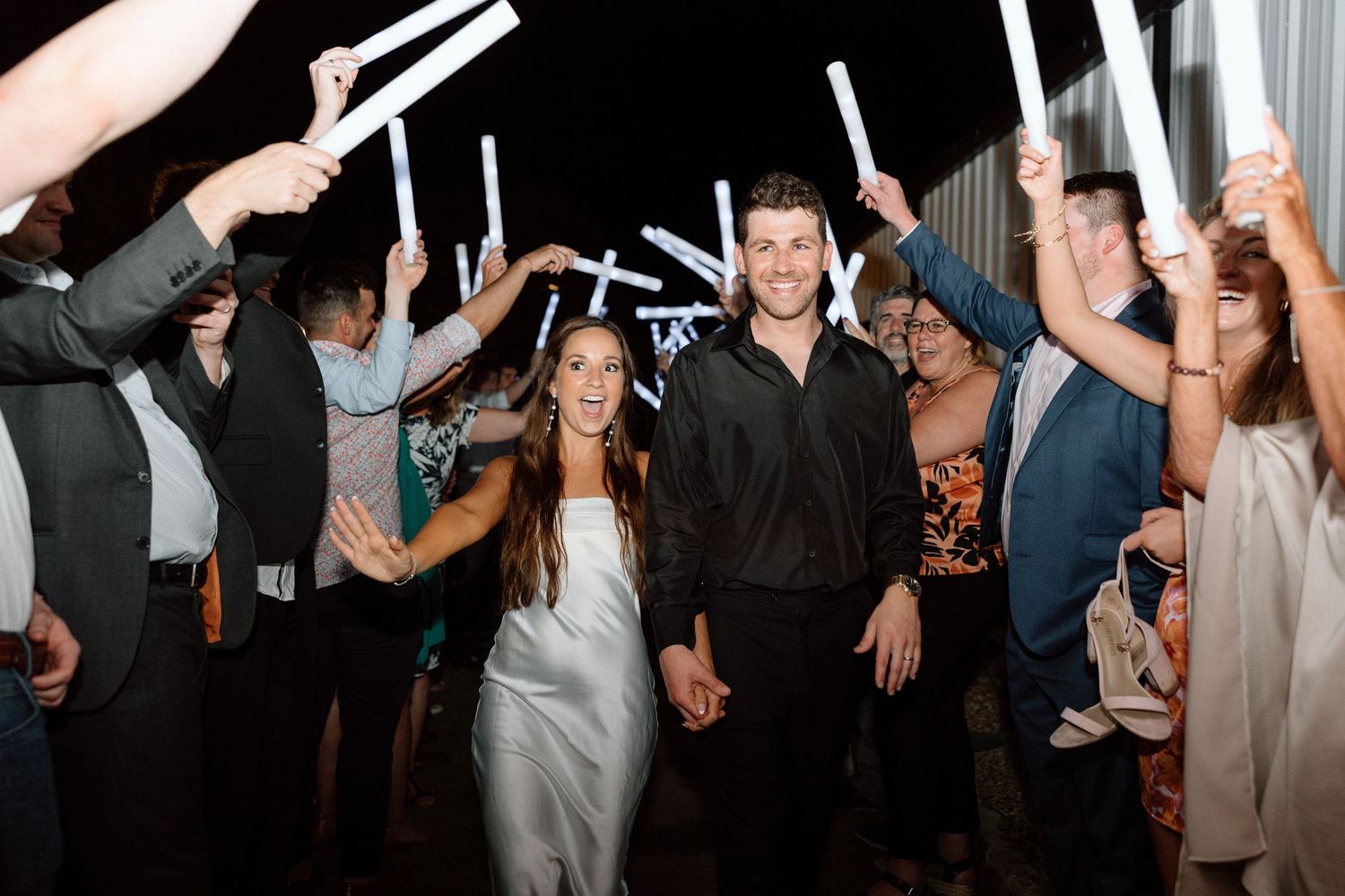 Wedding guests hold up light sticks to create a tunnel as a couple walks through during their reception celebration.