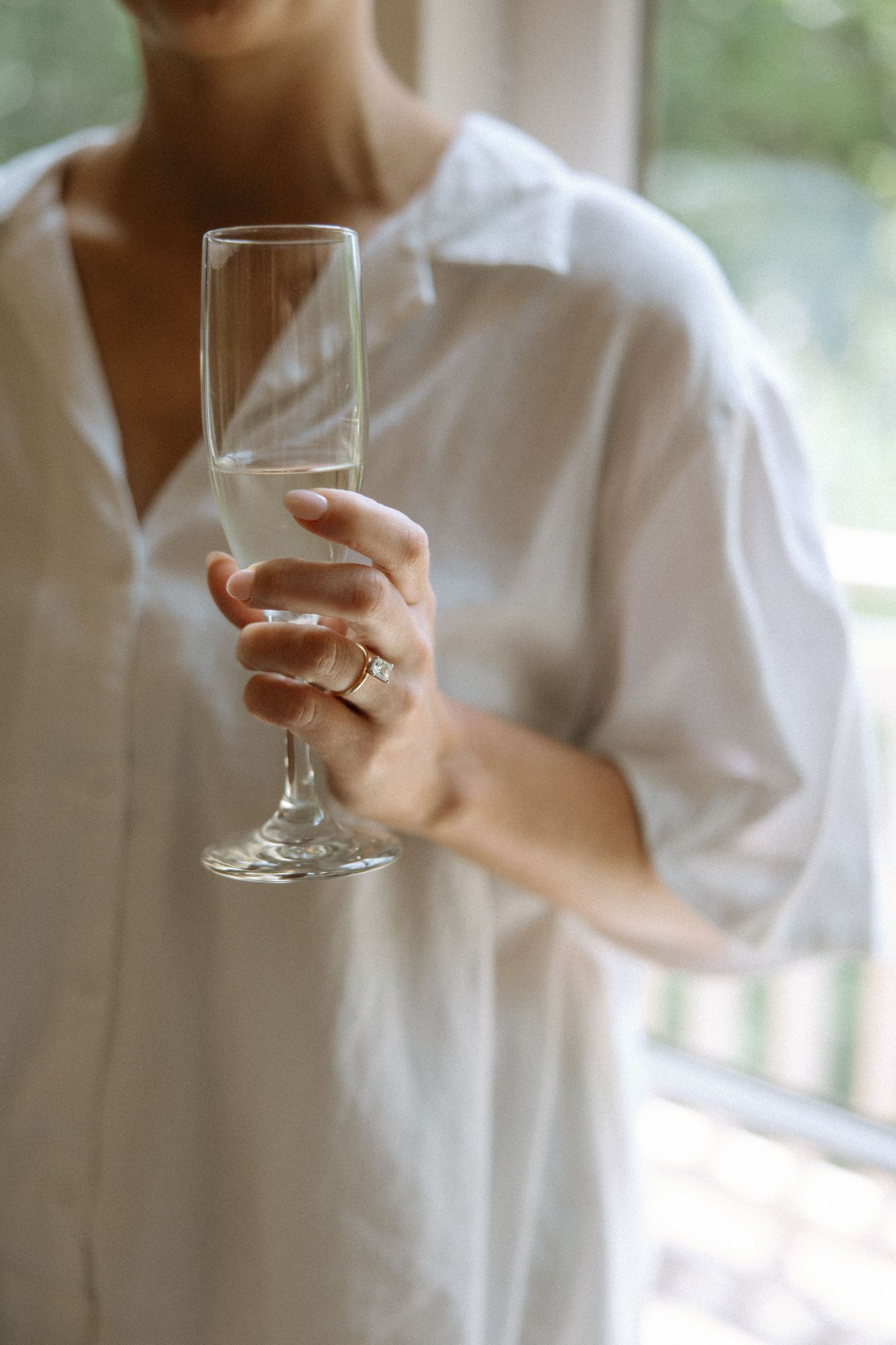 Person in white shirt holding a wine glass in soft natural light against blurred background.