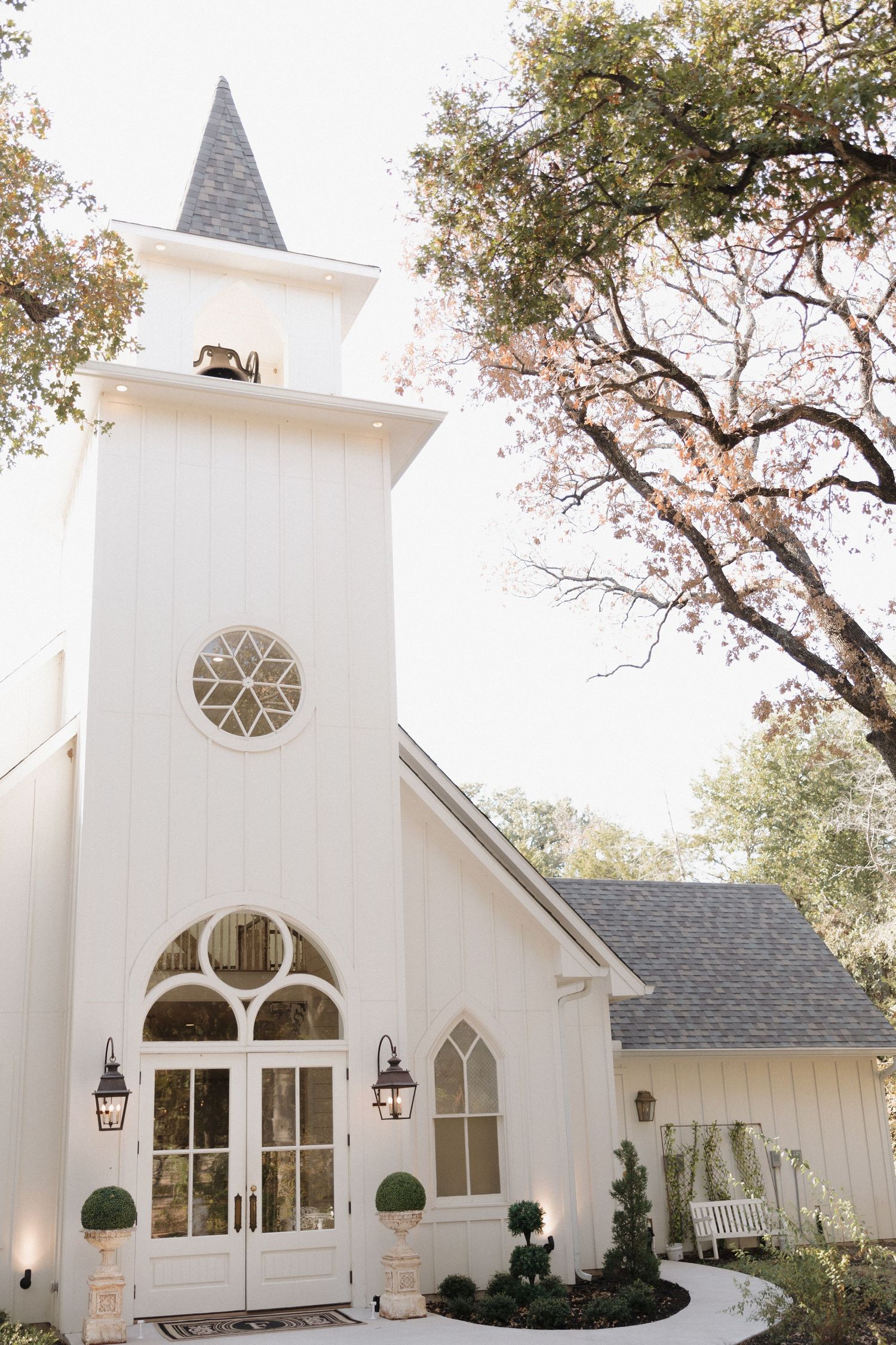 White chapel exterior with Gothic windows and twin spires showcases elegant wedding venue architecture in natural setting.