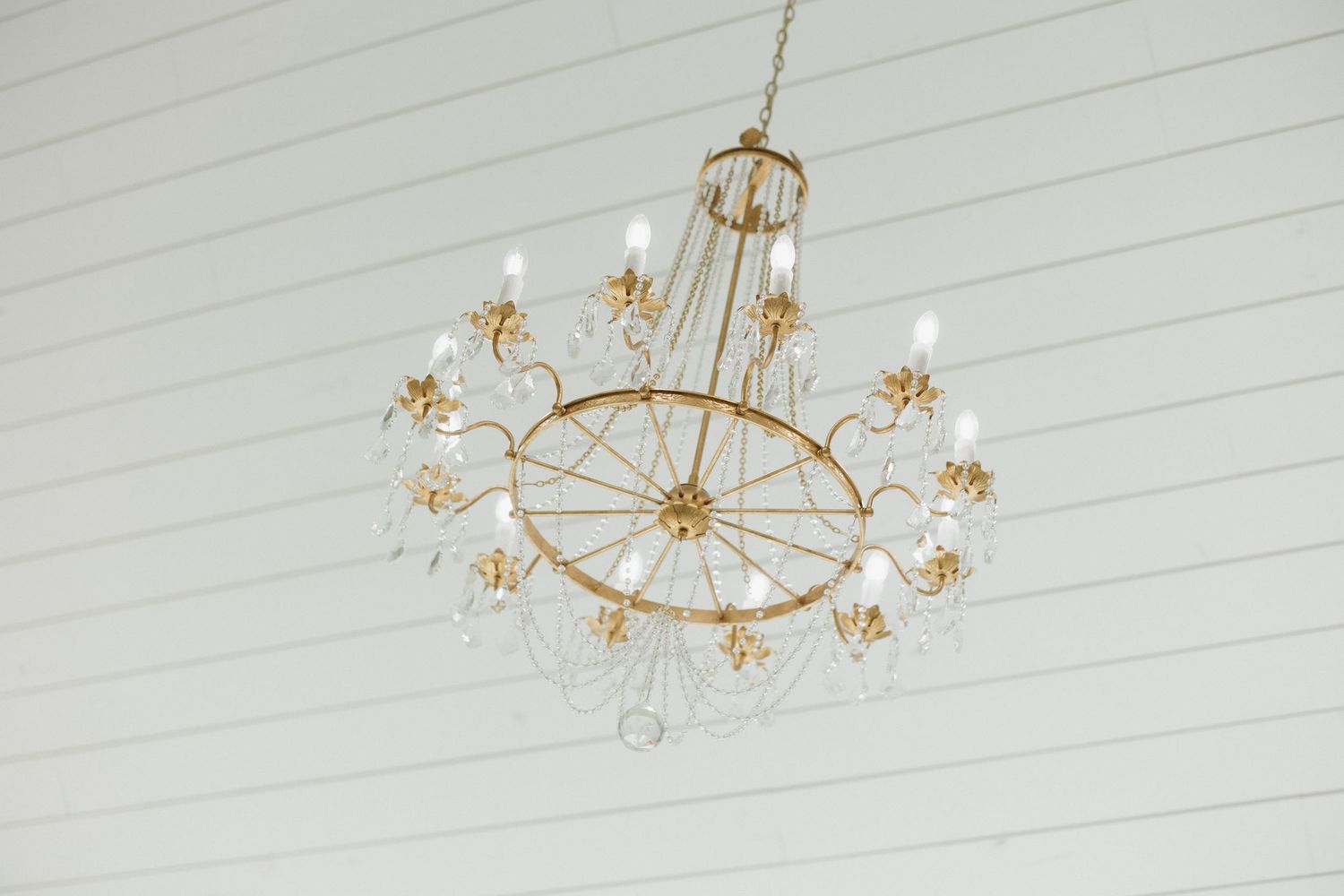 Modern gold and crystal sputnik chandelier with starburst design mounted on white shiplap ceiling.