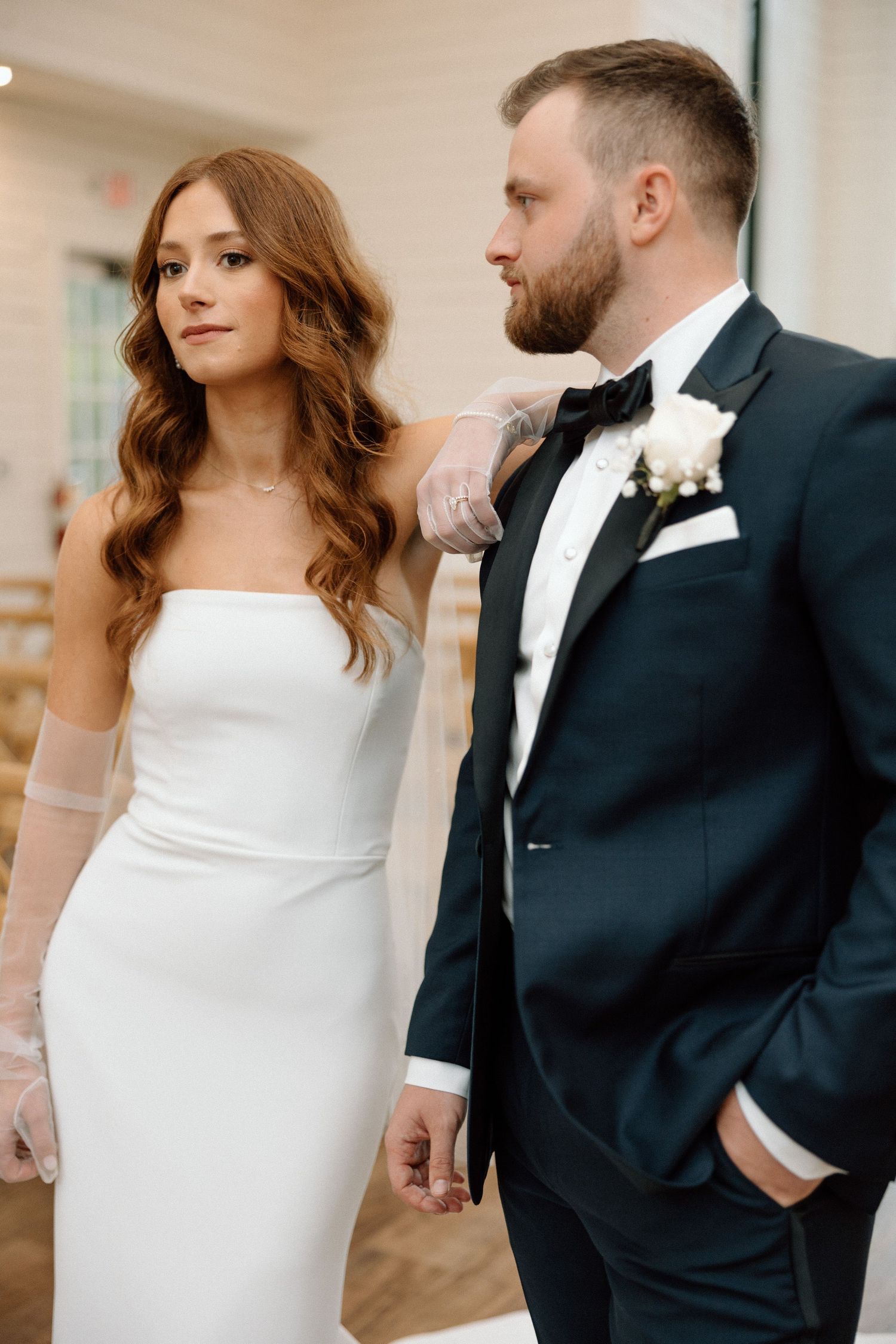 Elegant bride in strapless white gown poses with groom in black tuxedo during wedding photoshoot.