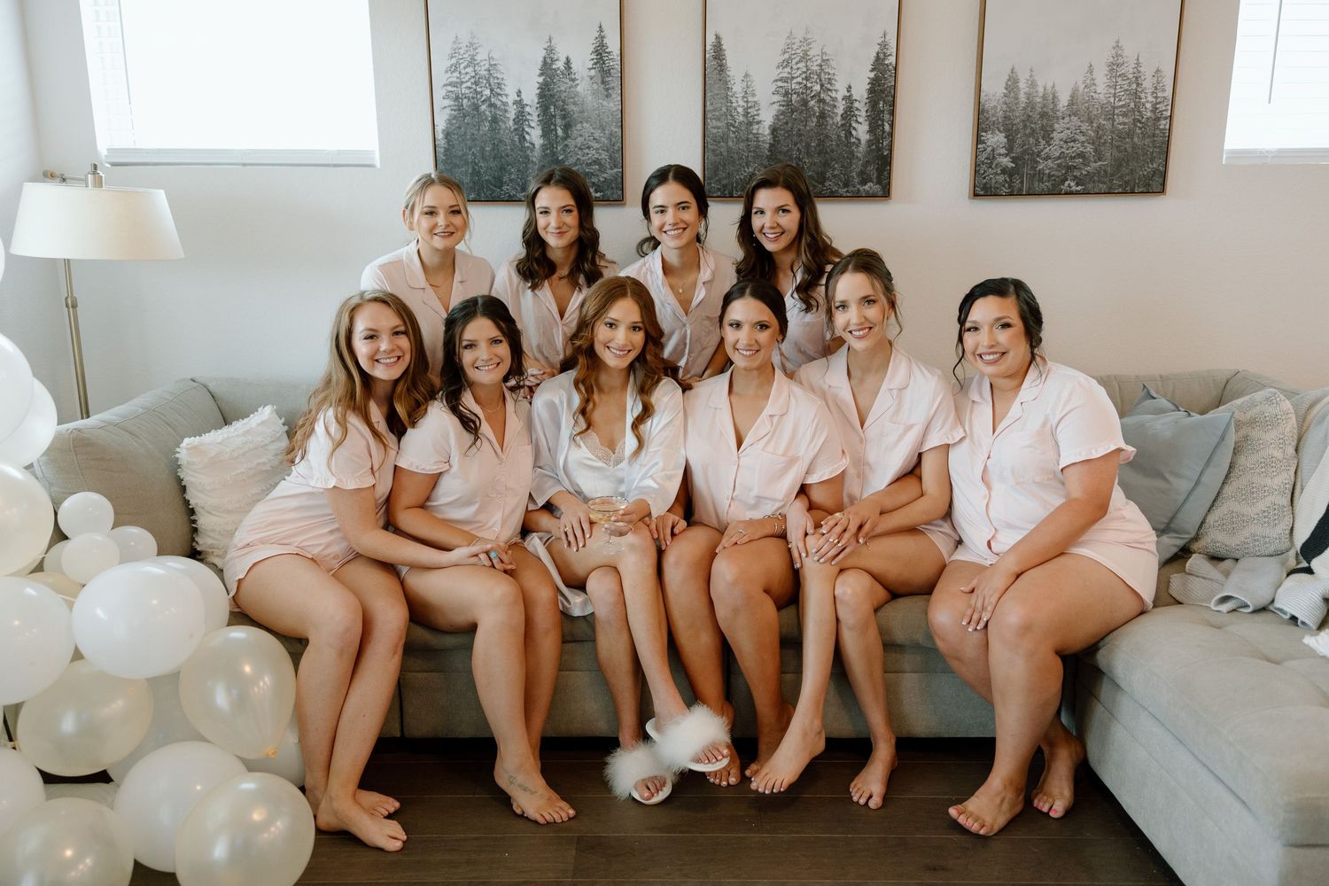 A group wearing matching pink and white robes sits together on a gray couch with white balloons for a celebration.