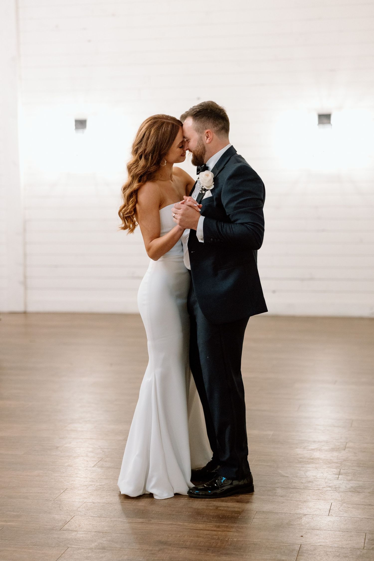 A couple shares their first dance in a minimalist white studio space, captured in a romantic sequence of photos.