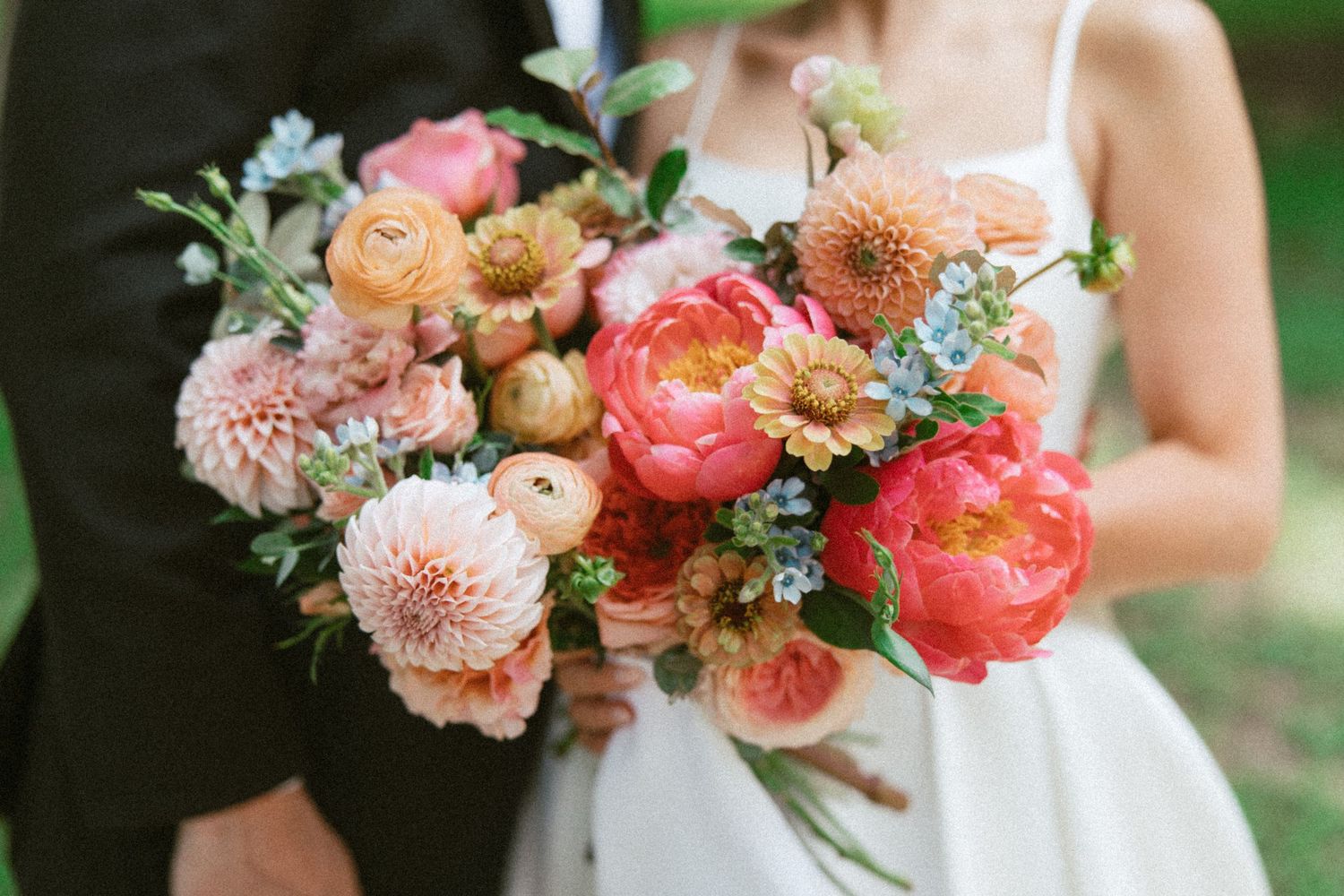 A row of coral and peach colored wedding bouquets with dahlias, roses and eucalyptus against a garden backdrop.