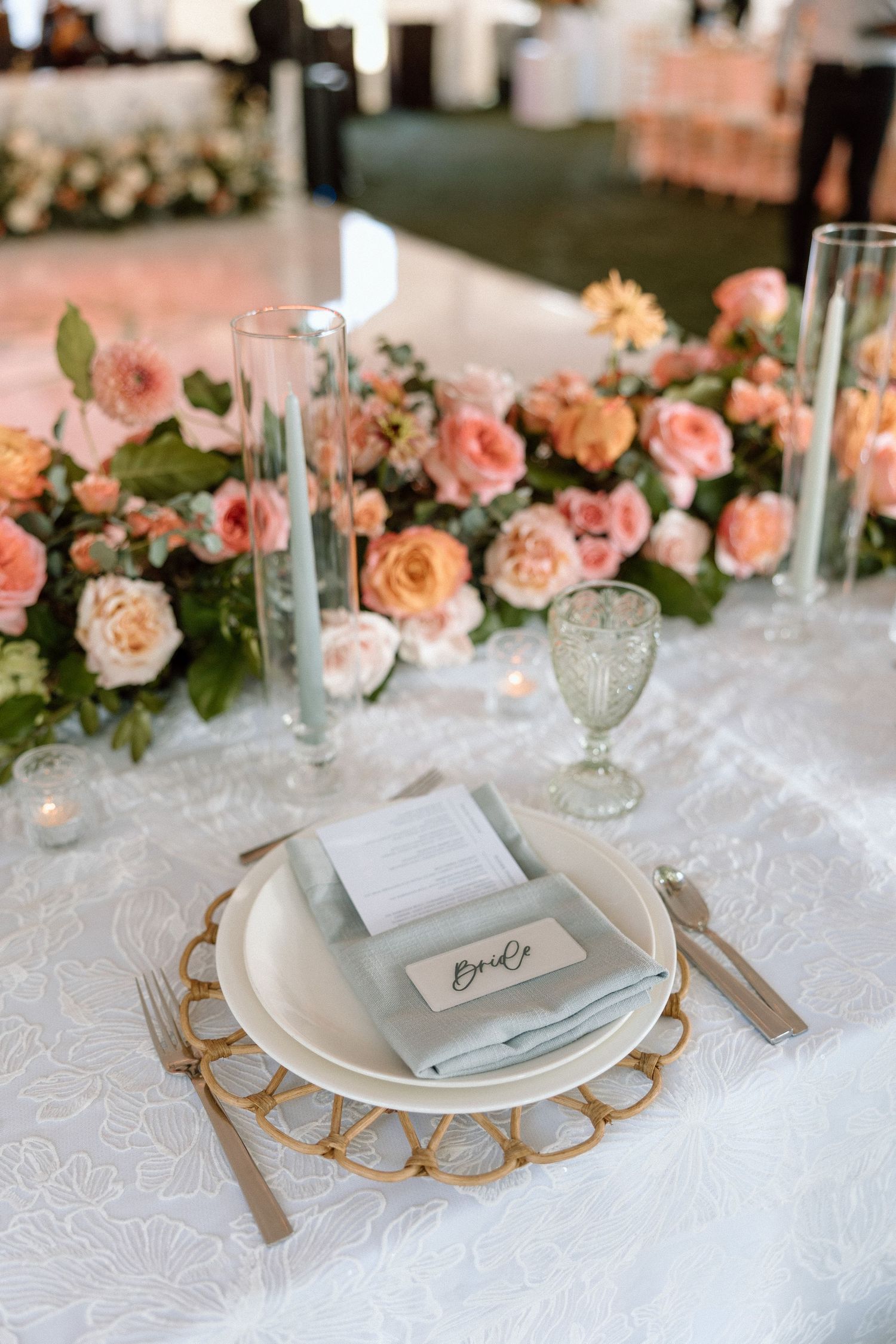 Elegant wedding table settings with white lace tablecloth, gold chargers, and coral roses as centerpiece decorations.