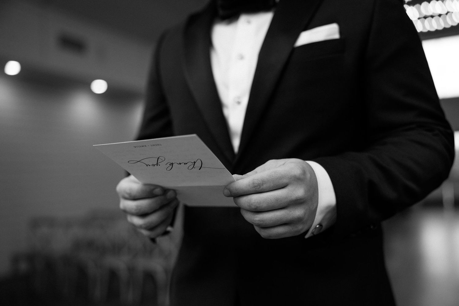 Black and white image of hands in formal attire holding a folded paper note or letter.