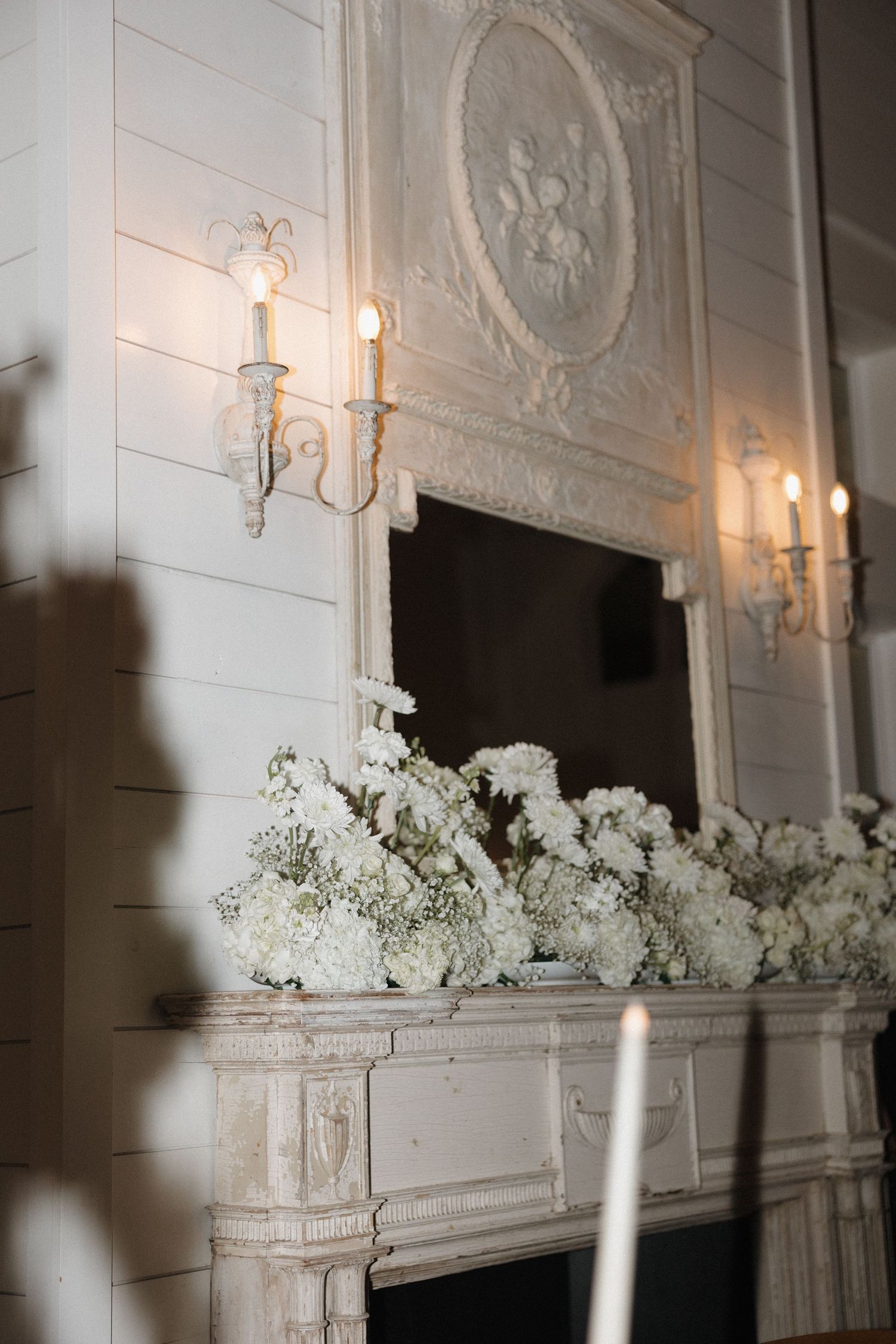Elegant white mantel decorated with hydrangeas and candle sconces in a formal room setting.