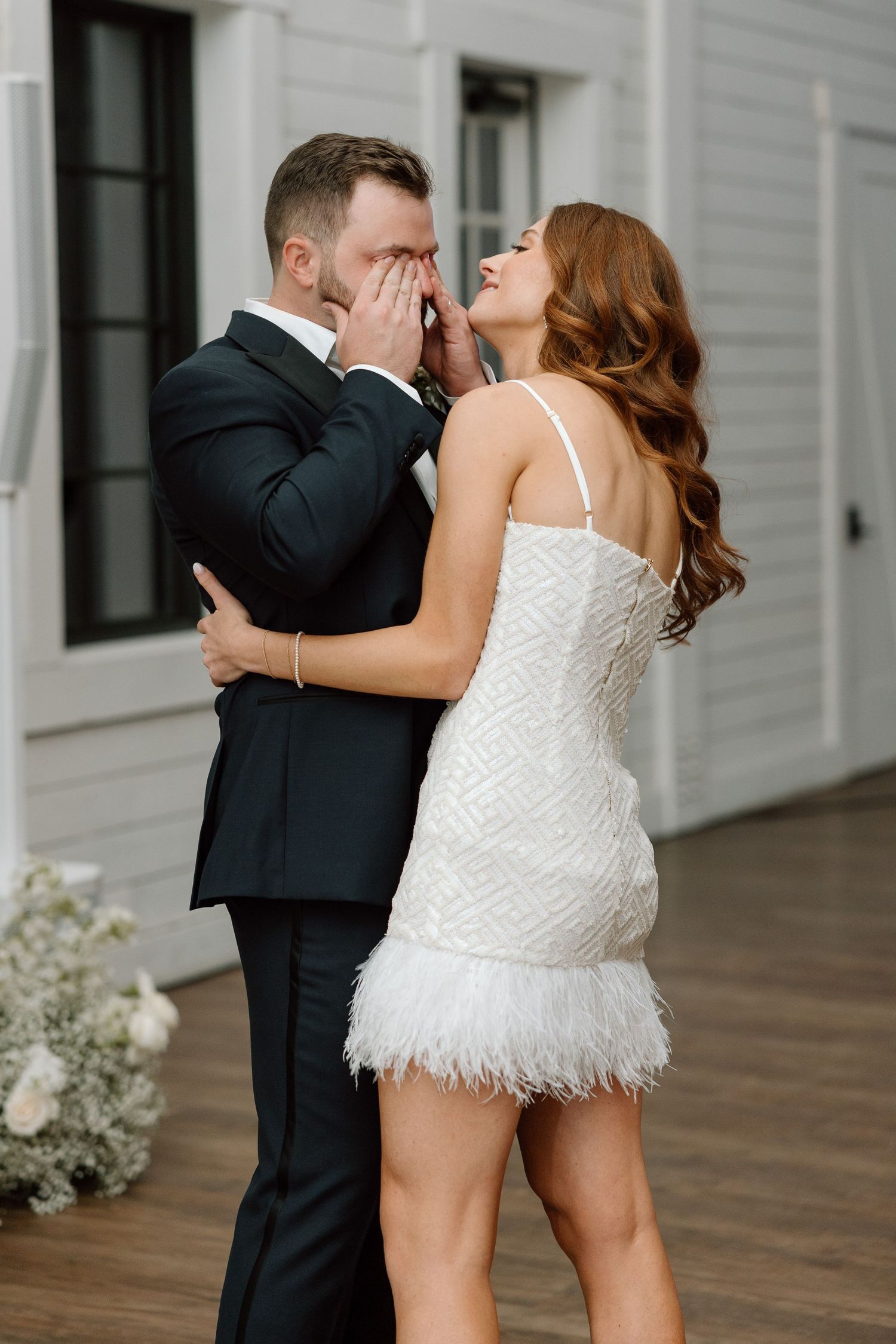 A couple in wedding attire shares intimate dance moves on a wooden porch in front of a white building.