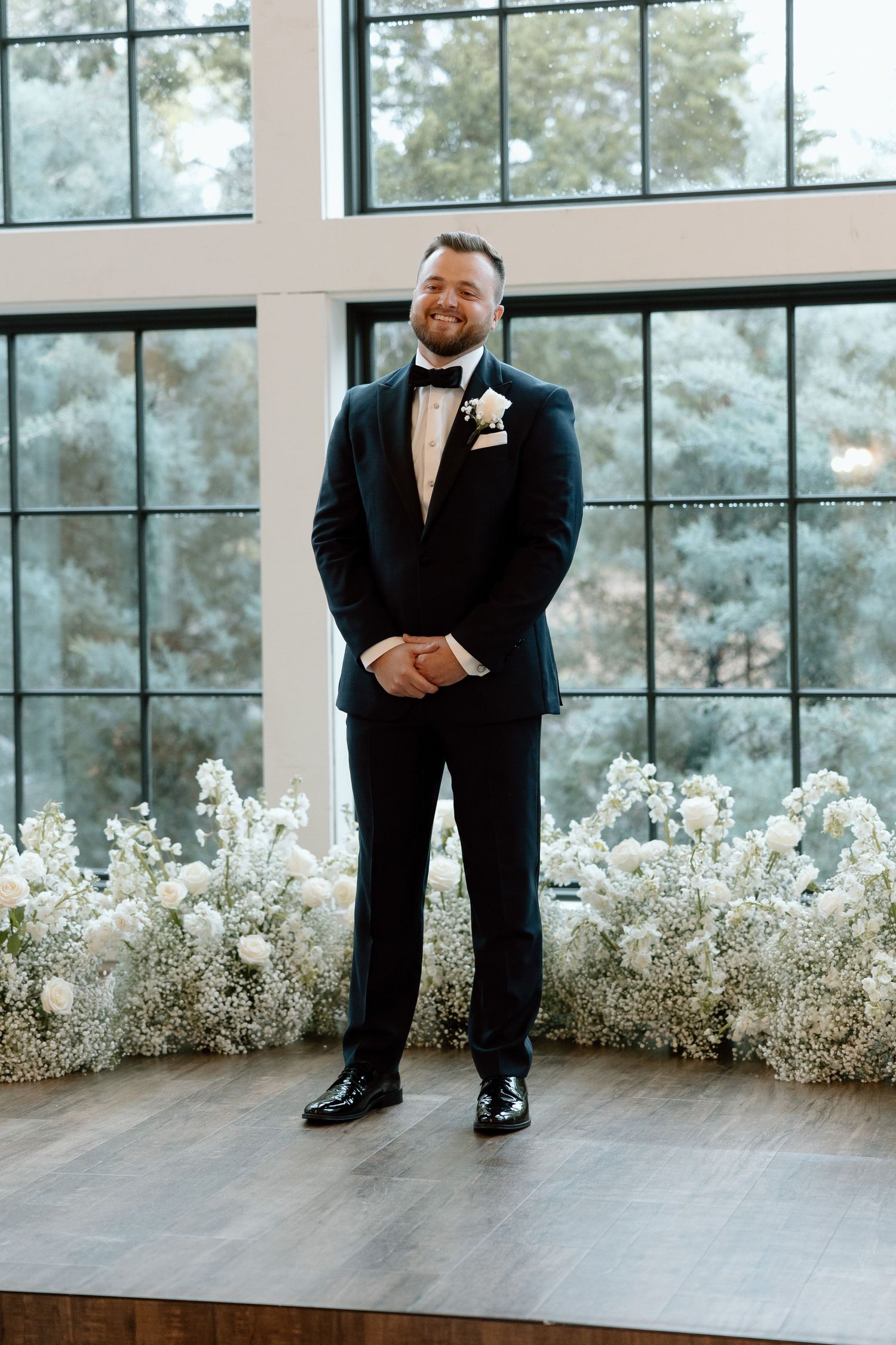 A series of four wedding photos showing a groom's black dress shoes and pants against a backdrop of white floral arrangements.
