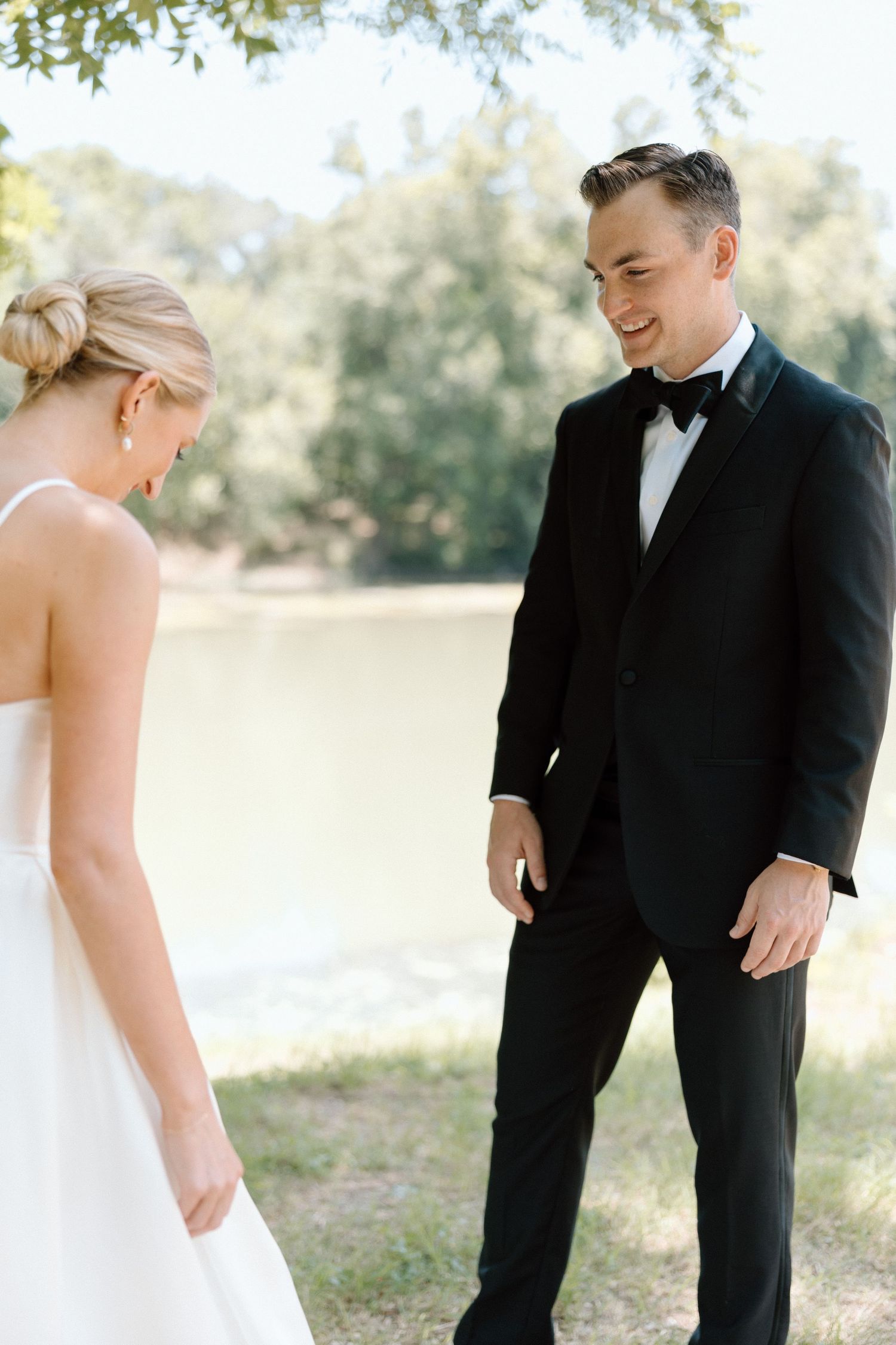 A bride and groom share a romantic moment outdoors during their wedding photo session near a lake.