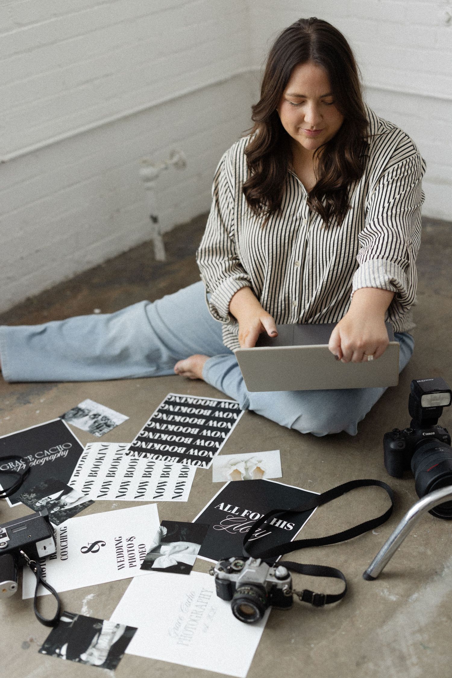 Content creator sitting cross-legged on floor with laptop, cameras and typography materials spread around them.