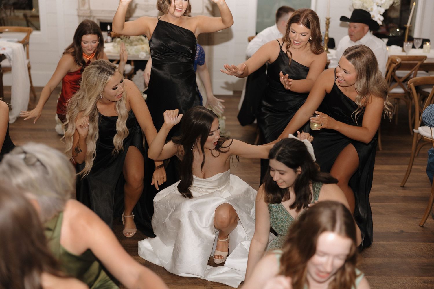 Wedding guests dance and celebrate on a rustic wooden dance floor during a lively reception party.