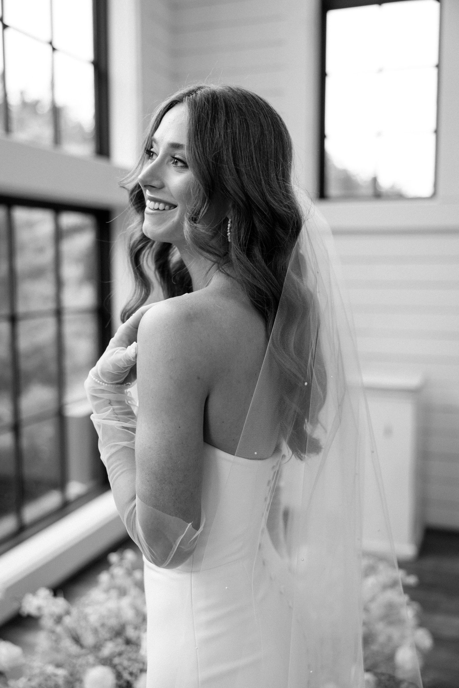A bride in a white wedding dress and veil looks out a window in a series of black and white candid shots.
