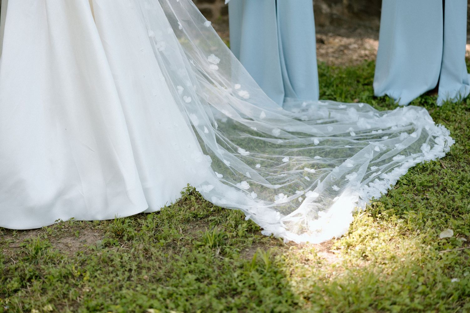 White wedding dress details with delicate lace and tulle fabric flowing over grass in an outdoor setting.