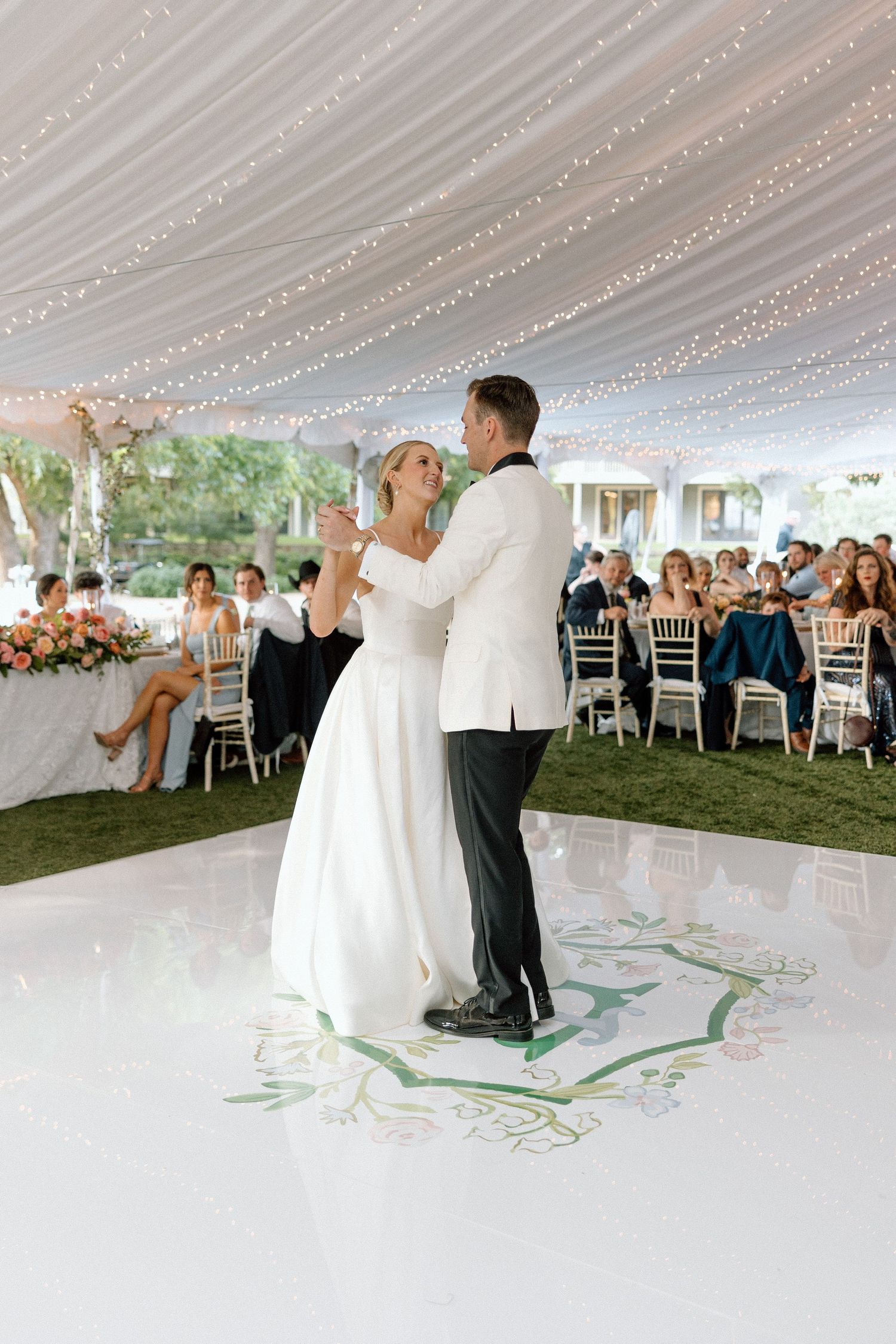 A couple shares their first dance under a draped tent ceiling with twinkling lights at an elegant outdoor wedding reception.