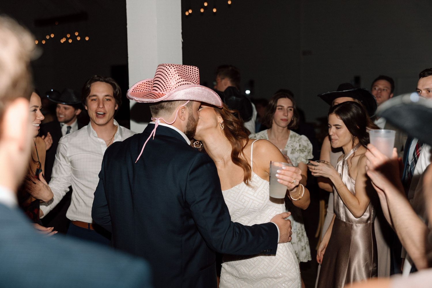 Wedding guests dancing and celebrating on the dance floor at a reception with someone wearing a pink cowboy hat.