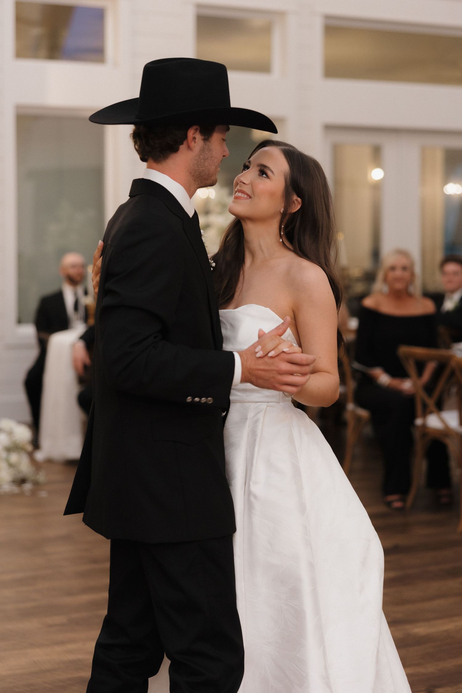A couple shares their first dance at a wedding reception in an elegant venue with hardwood floors.