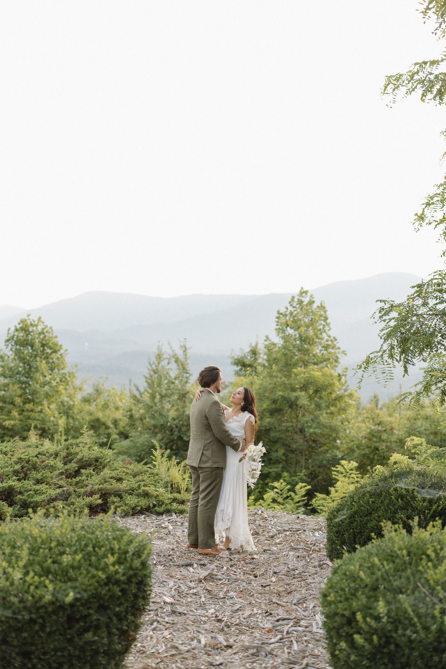 Romantic wedding couple standing on rocky overlook with mountain vista.