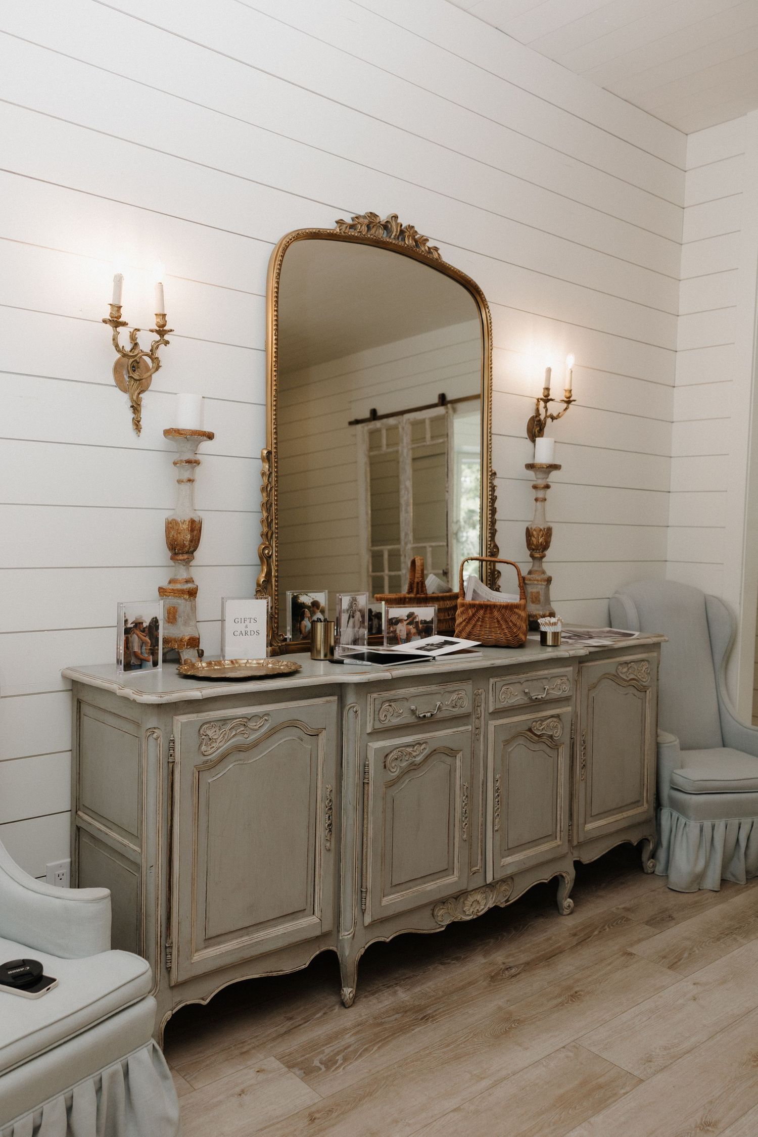 Elegant French country style sideboard with ornate mirror and wall sconces in a white shiplap room.