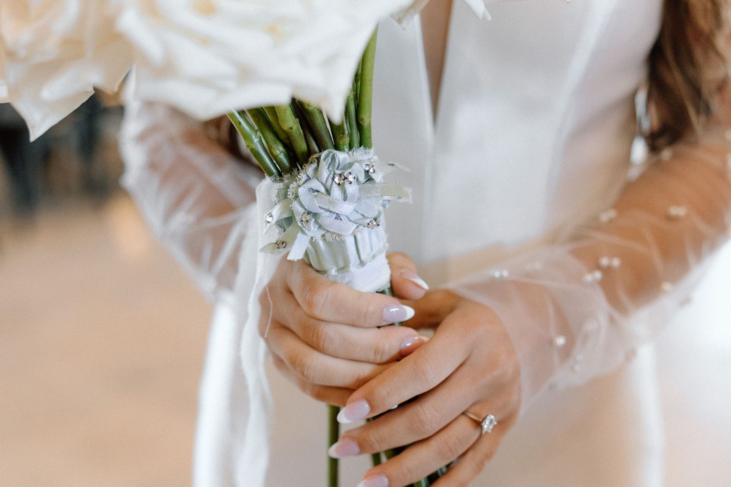Close-up of white bridal bouquet with delicate flowers and greenery being held by hands wearing rings.