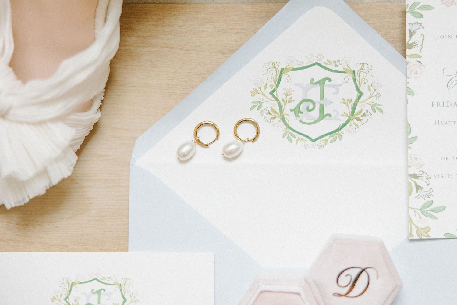 Wedding invitation suite with gold wedding rings and delicate green monogram on white envelope.