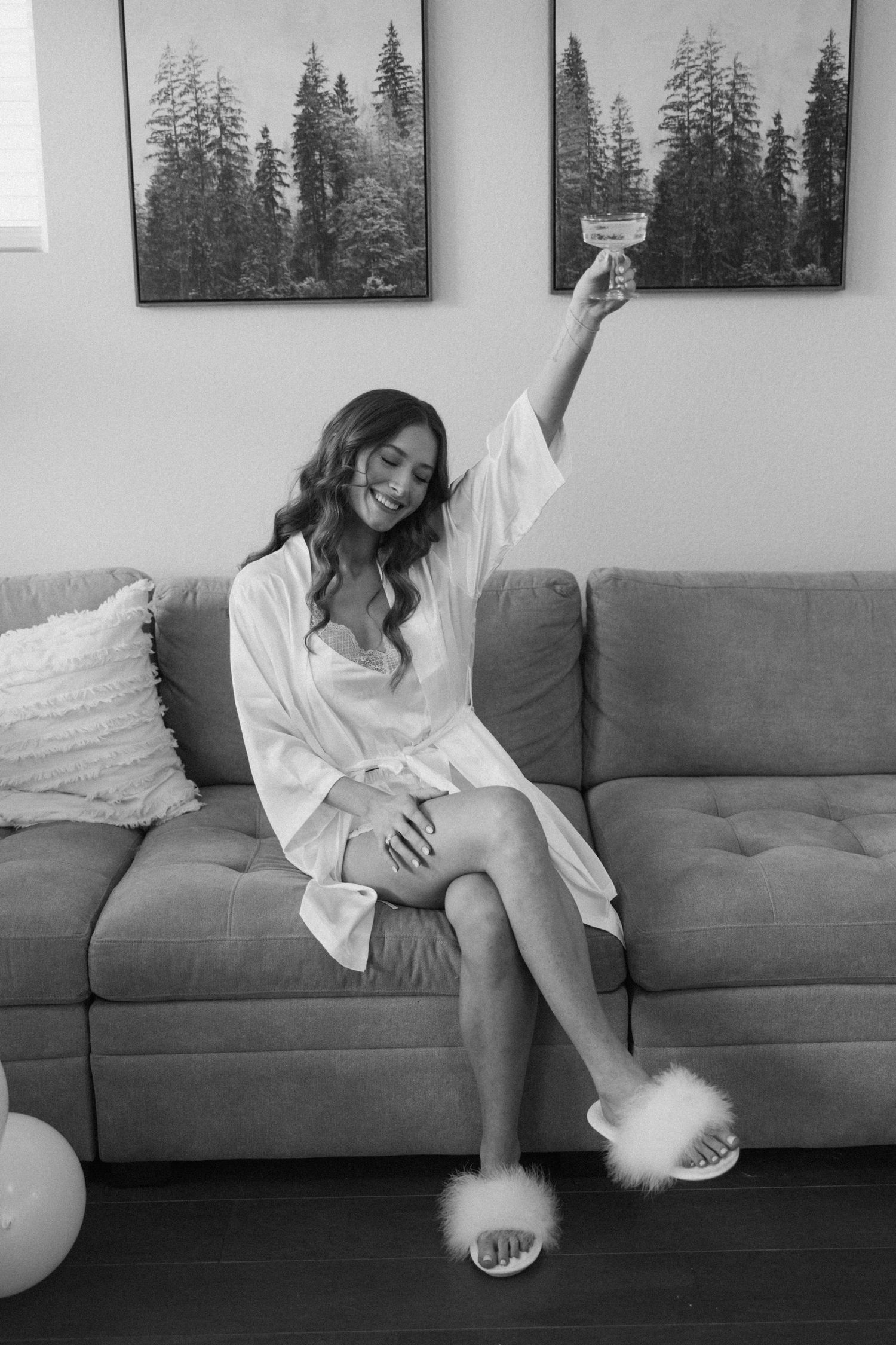 Black and white artistic photo series showing relaxed poses on a modern gray couch with forest artwork in background.