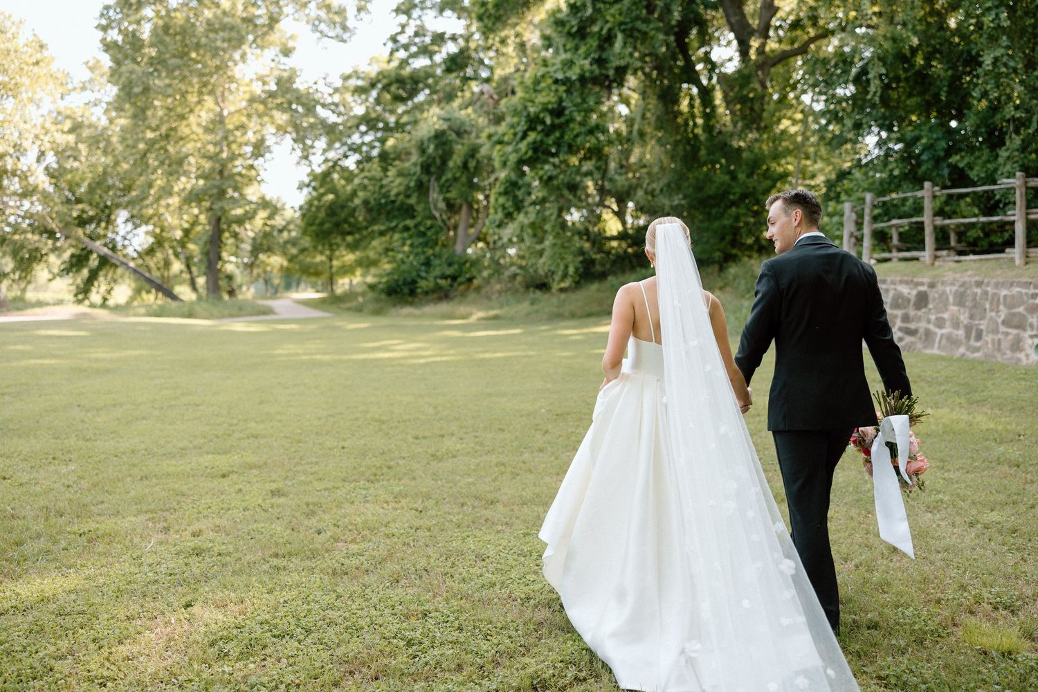 A romantic wedding couple walks together through a lush garden setting during their outdoor celebration.