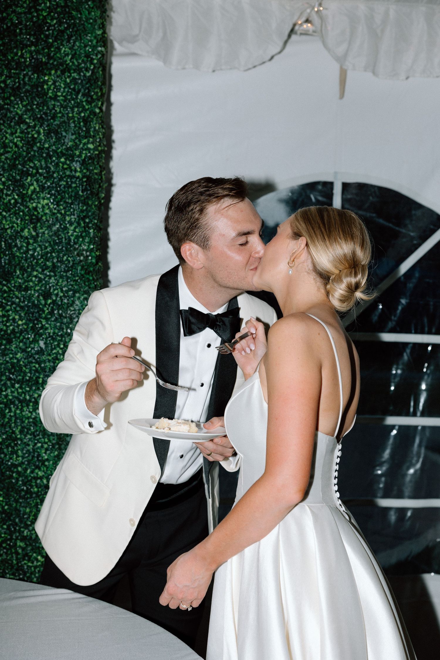 A couple in formal wedding attire sharing a romantic kiss sequence in front of a green hedge backdrop.