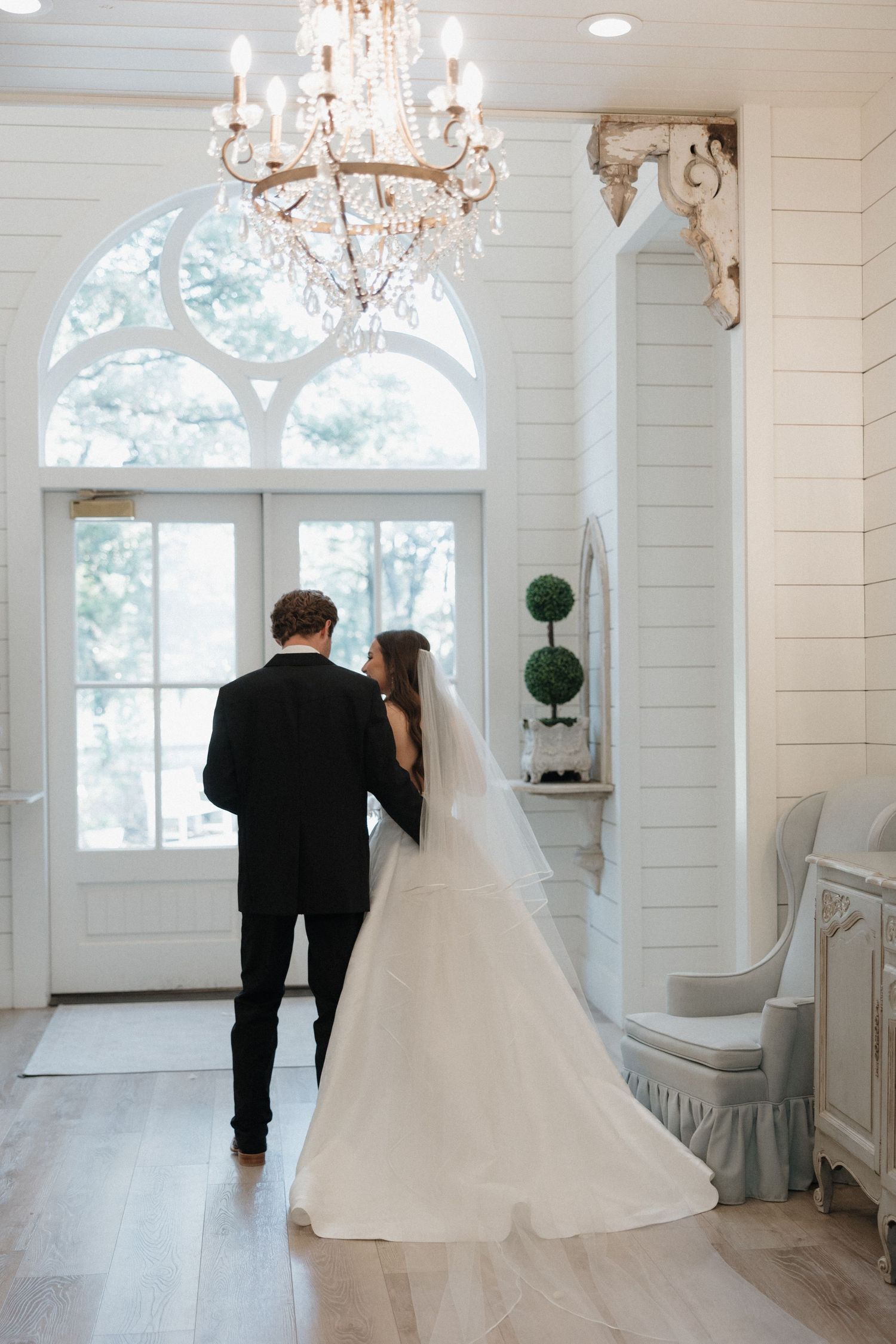 A series of elegant wedding photos showing a flowing white gown in a bright room with chandeliers and arched windows.