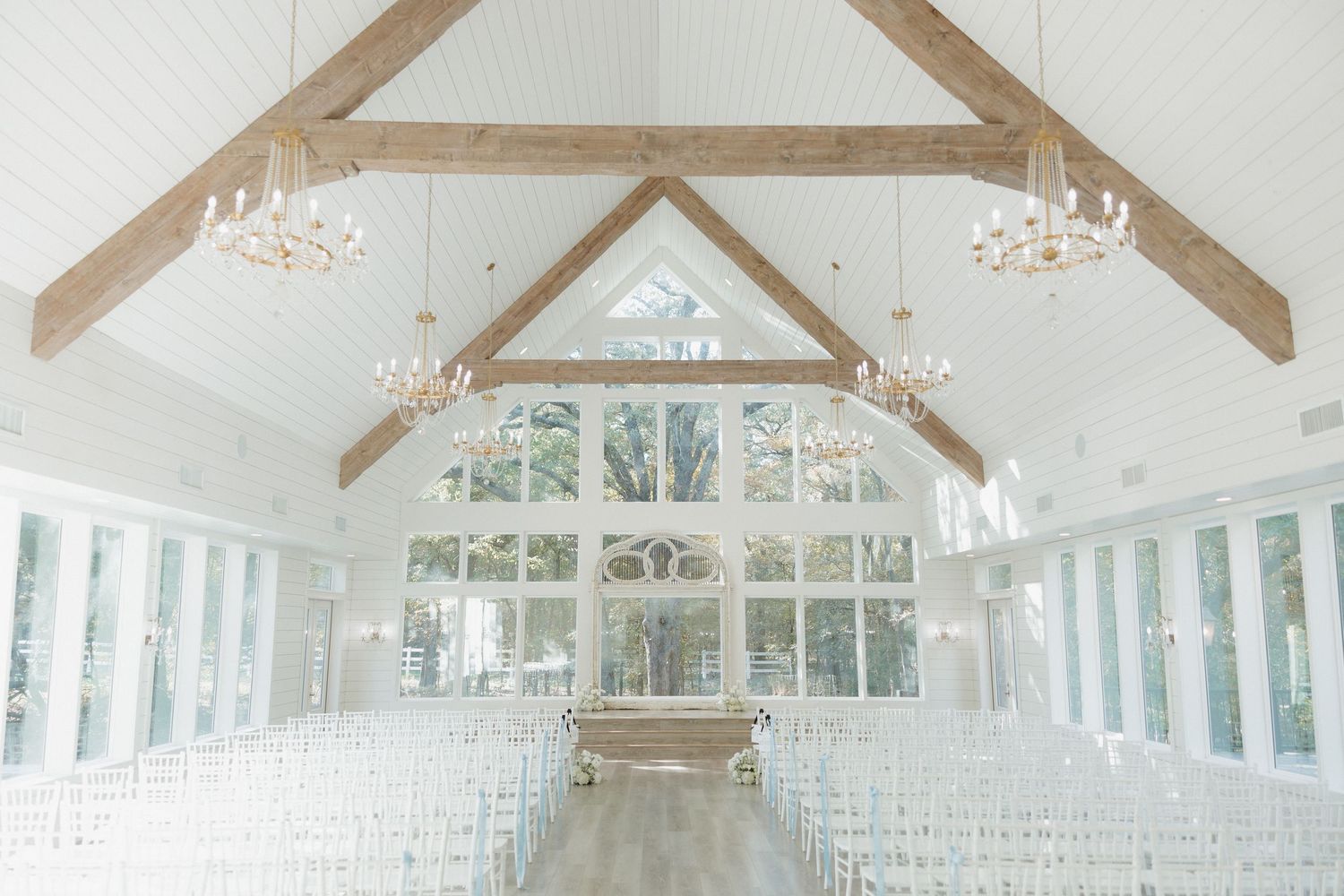 A bright white wedding venue with exposed wooden beams and large windows creating an elegant indoor space.