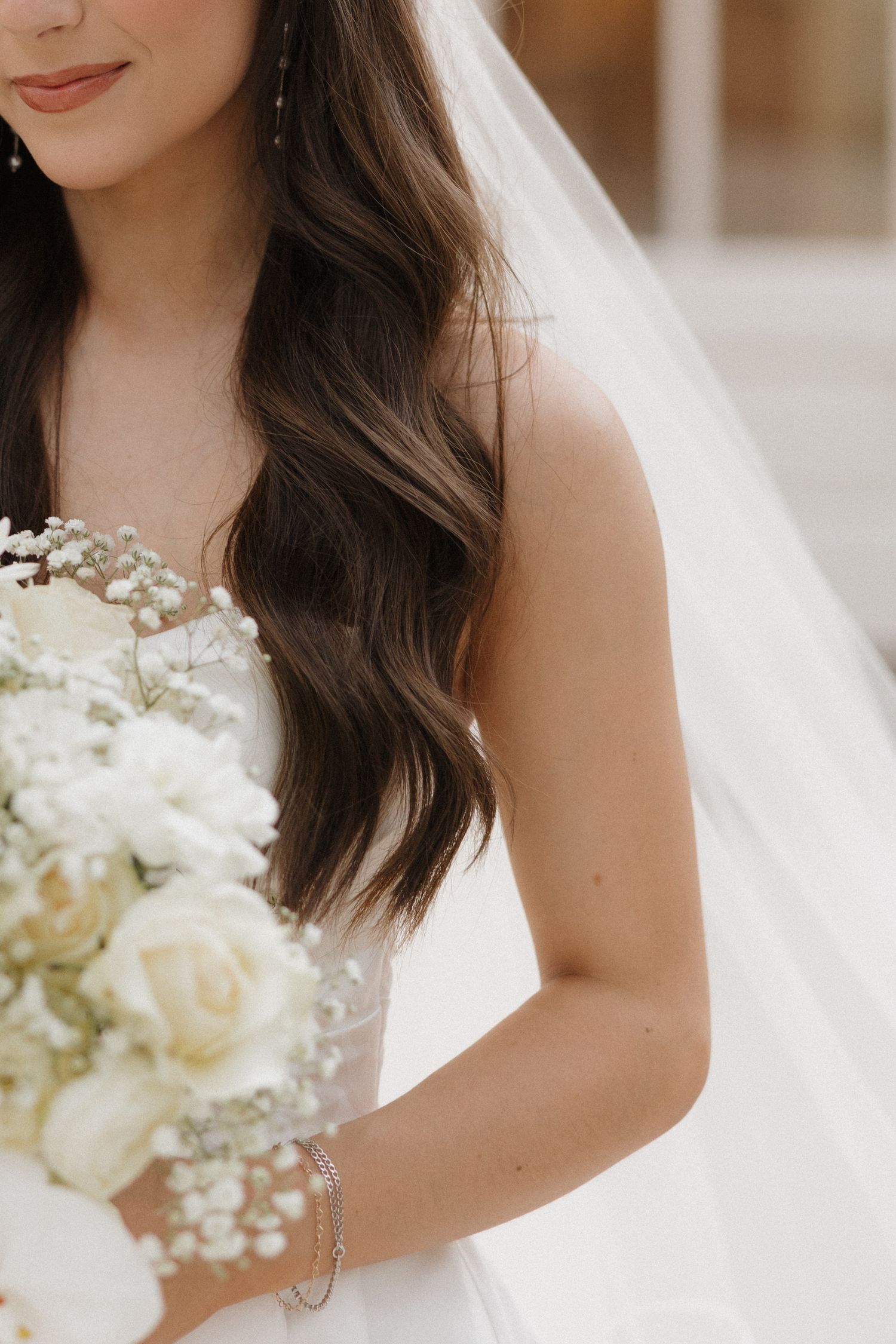 Close up detail of a bride holding a white floral bouquet with baby's breath against her white wedding dress.