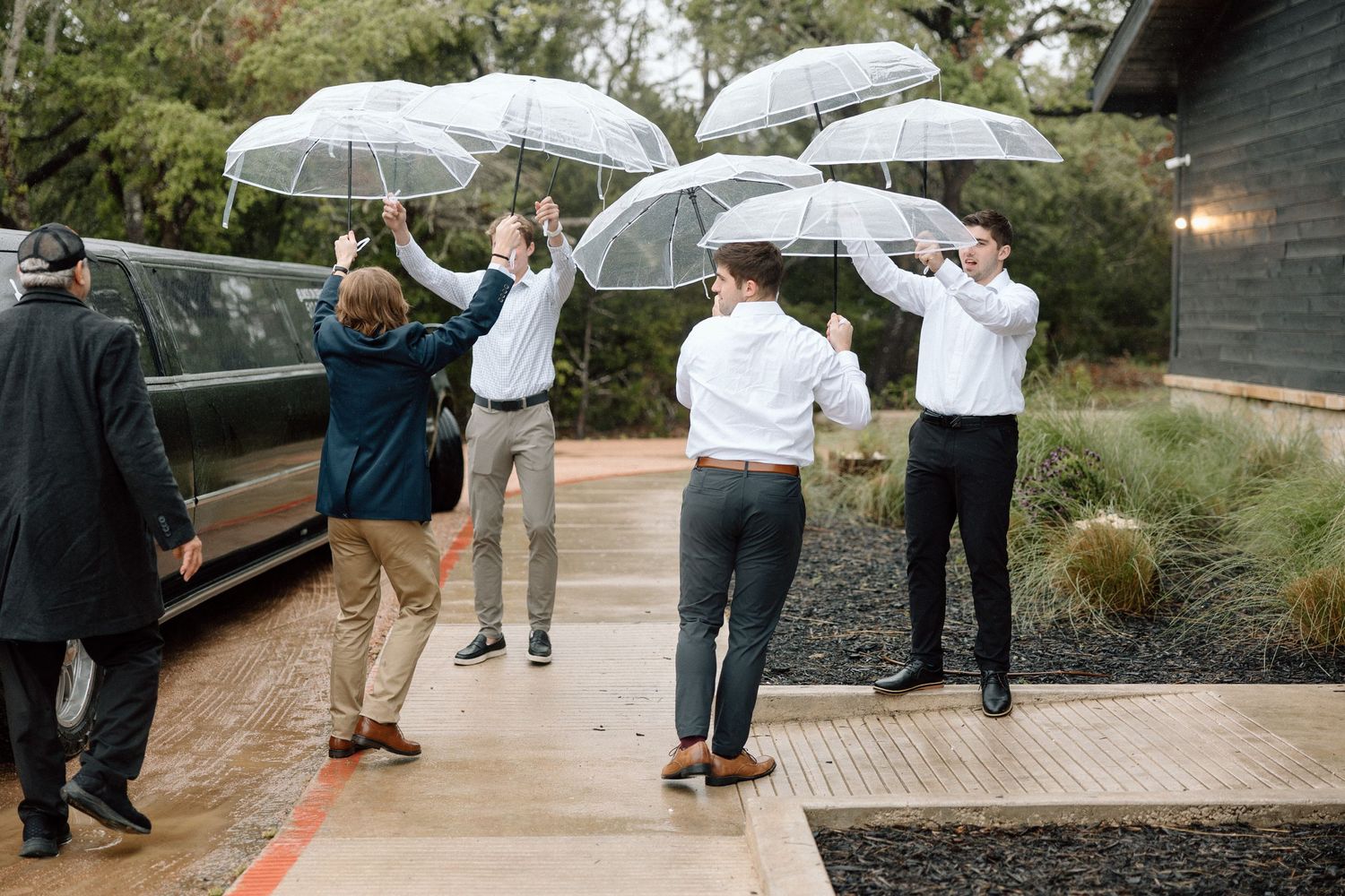 People holding clear umbrellas stand in a line outdoors during a rainy event.