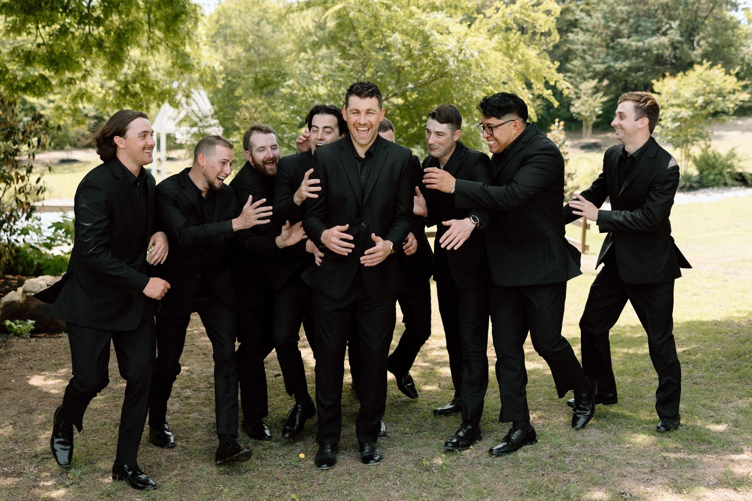 A sequence of people in black formal attire performing coordinated dance moves in an outdoor garden setting.