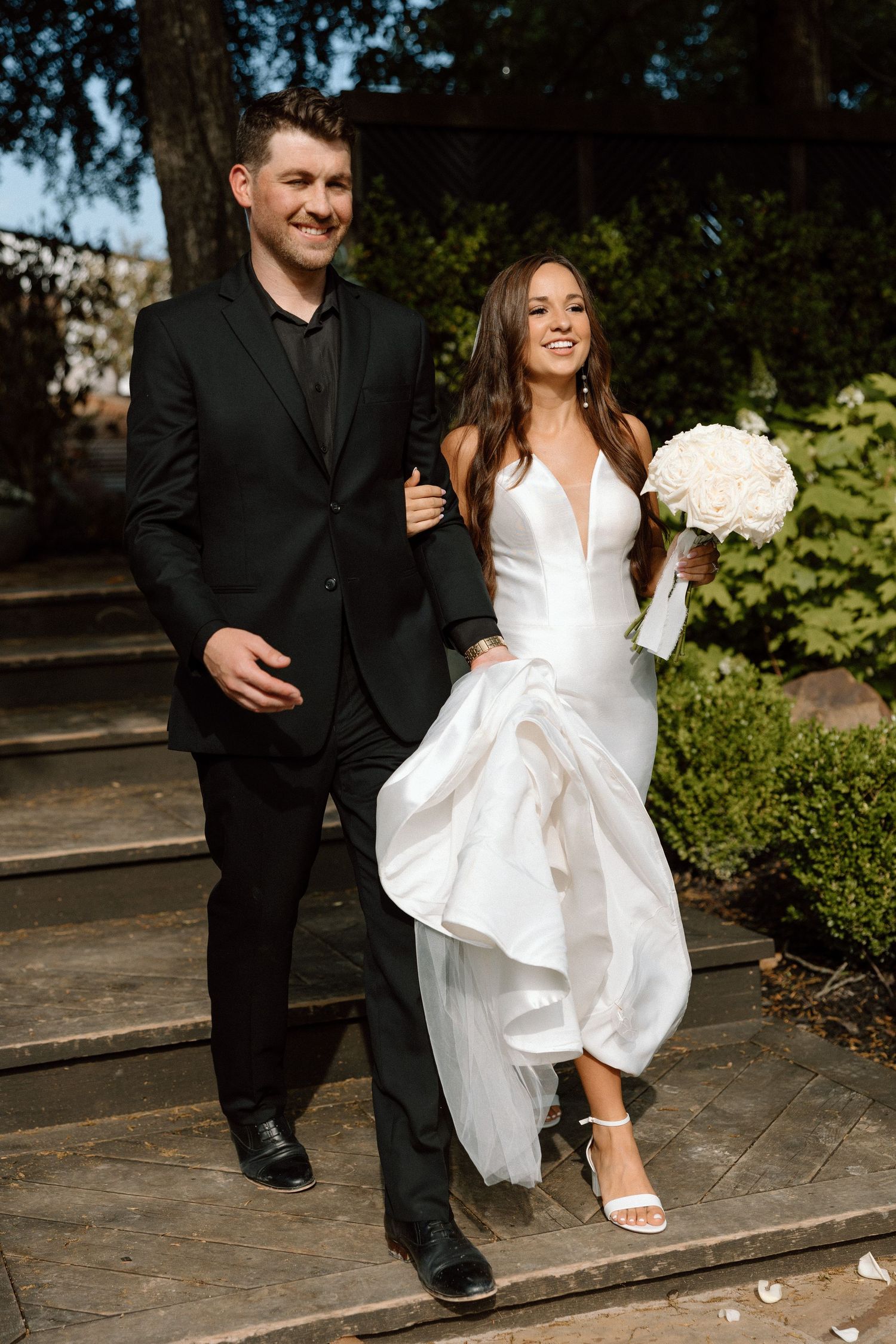Couple sitting on stone steps in formal wedding attire with bride wearing white dress and groom in black suit.