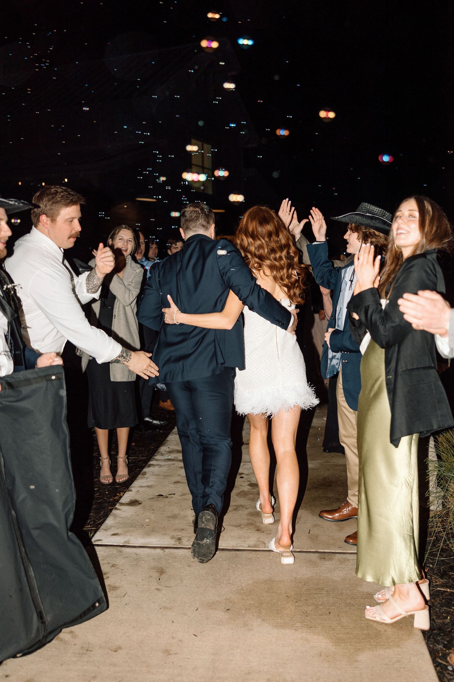 People dancing and celebrating at a nighttime party with festive lights glowing overhead.