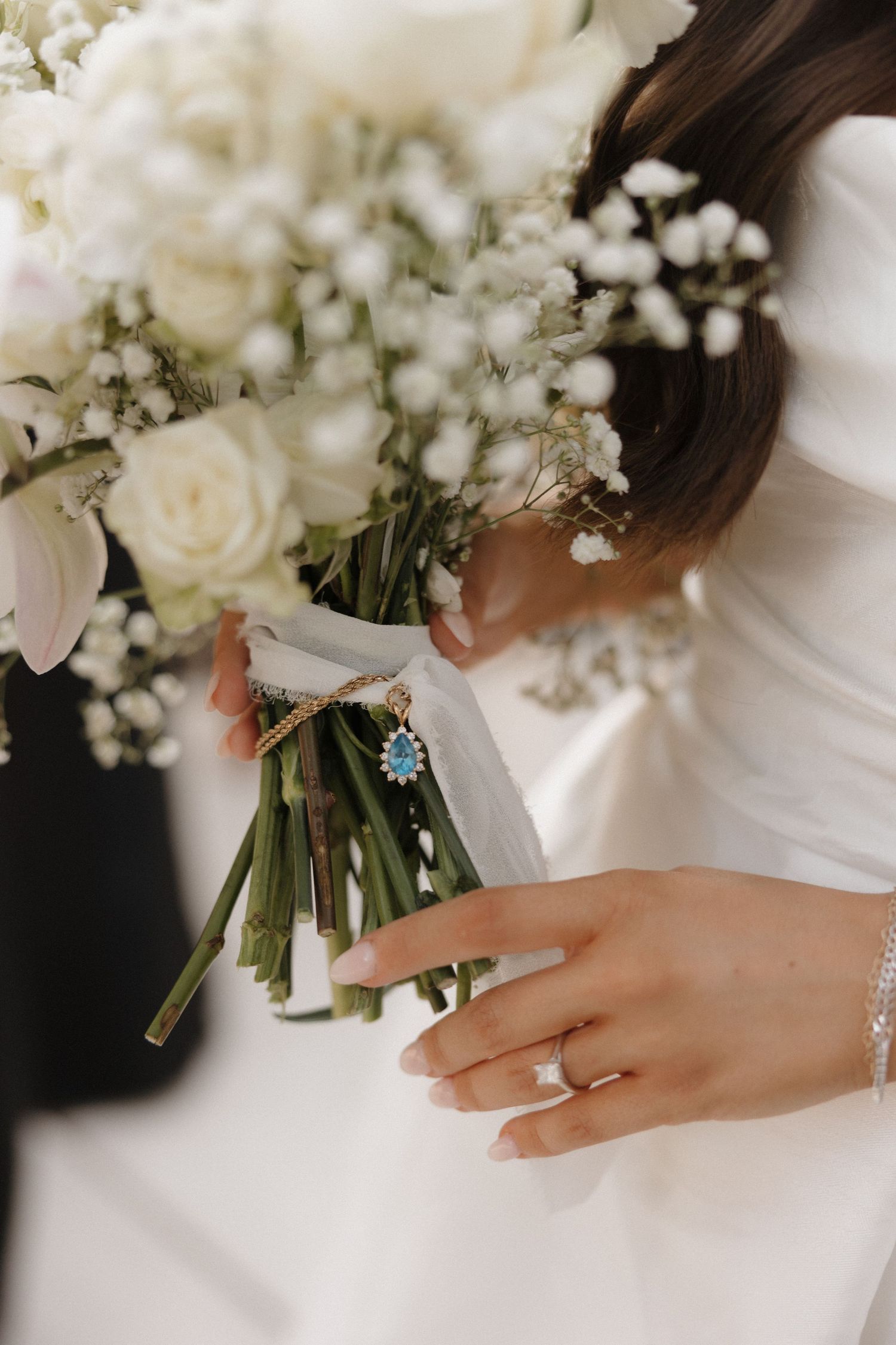 Close-up view of hands holding a white floral wedding bouquet with roses and baby's breath tied with ribbon.