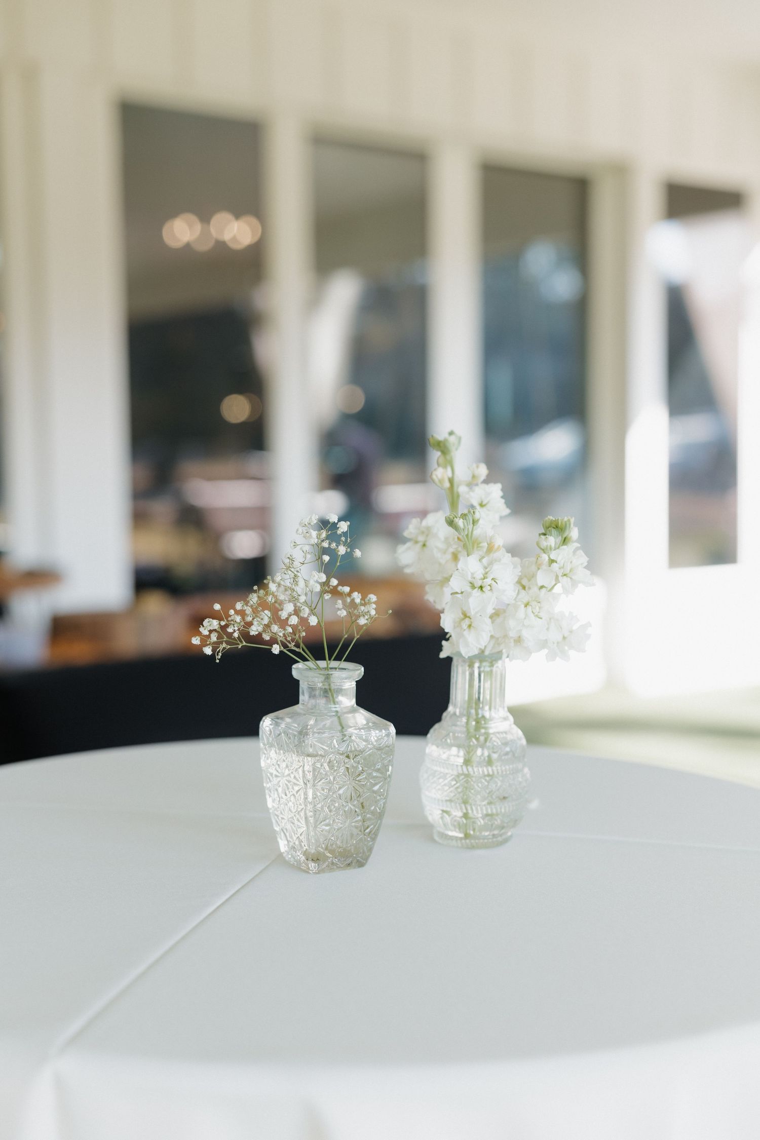 Small glass vases with delicate white baby's breath flowers arranged on a white surface in a minimalist style.
