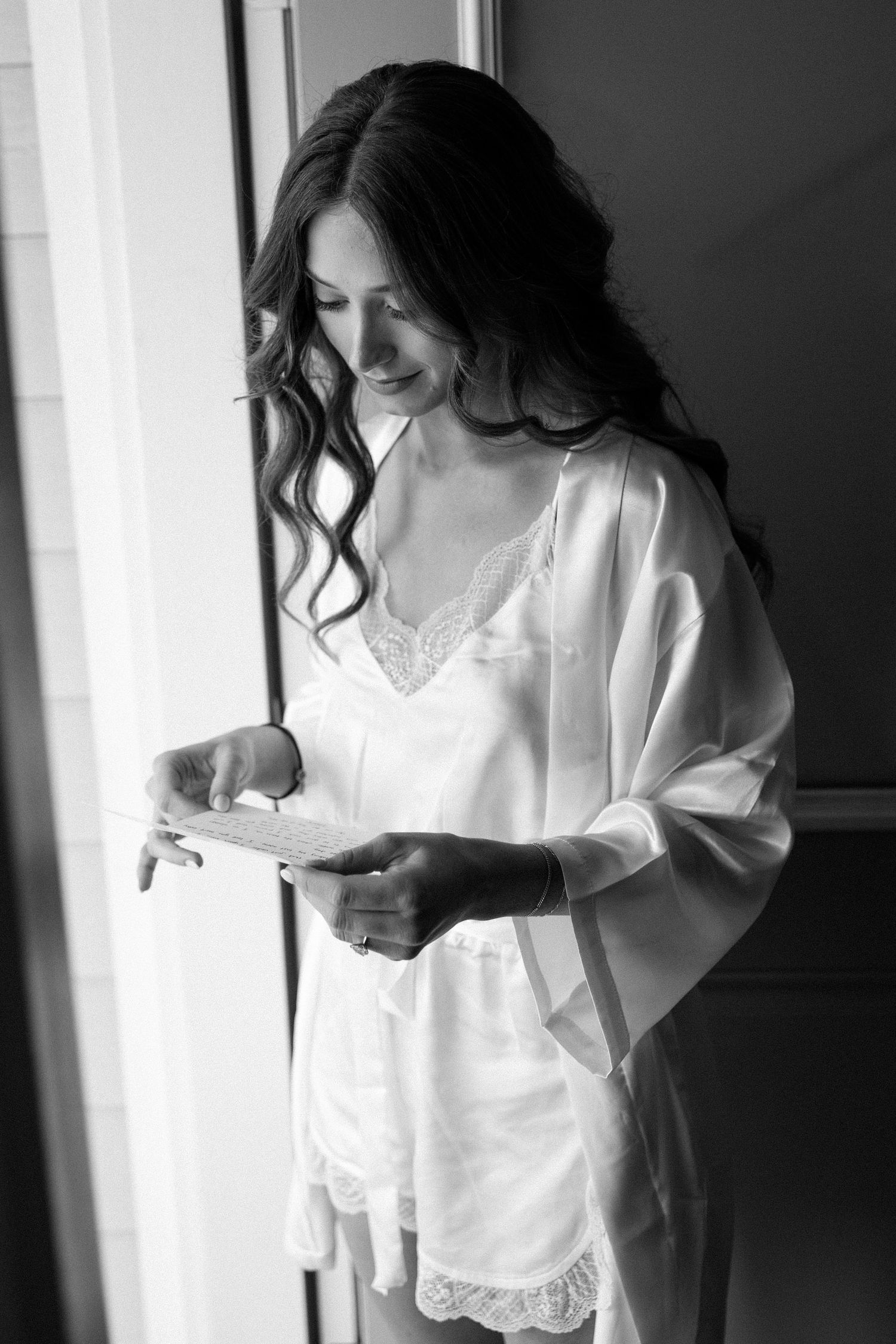 A woman in a white dress stands by a window in a series of black and white artistic portraits.