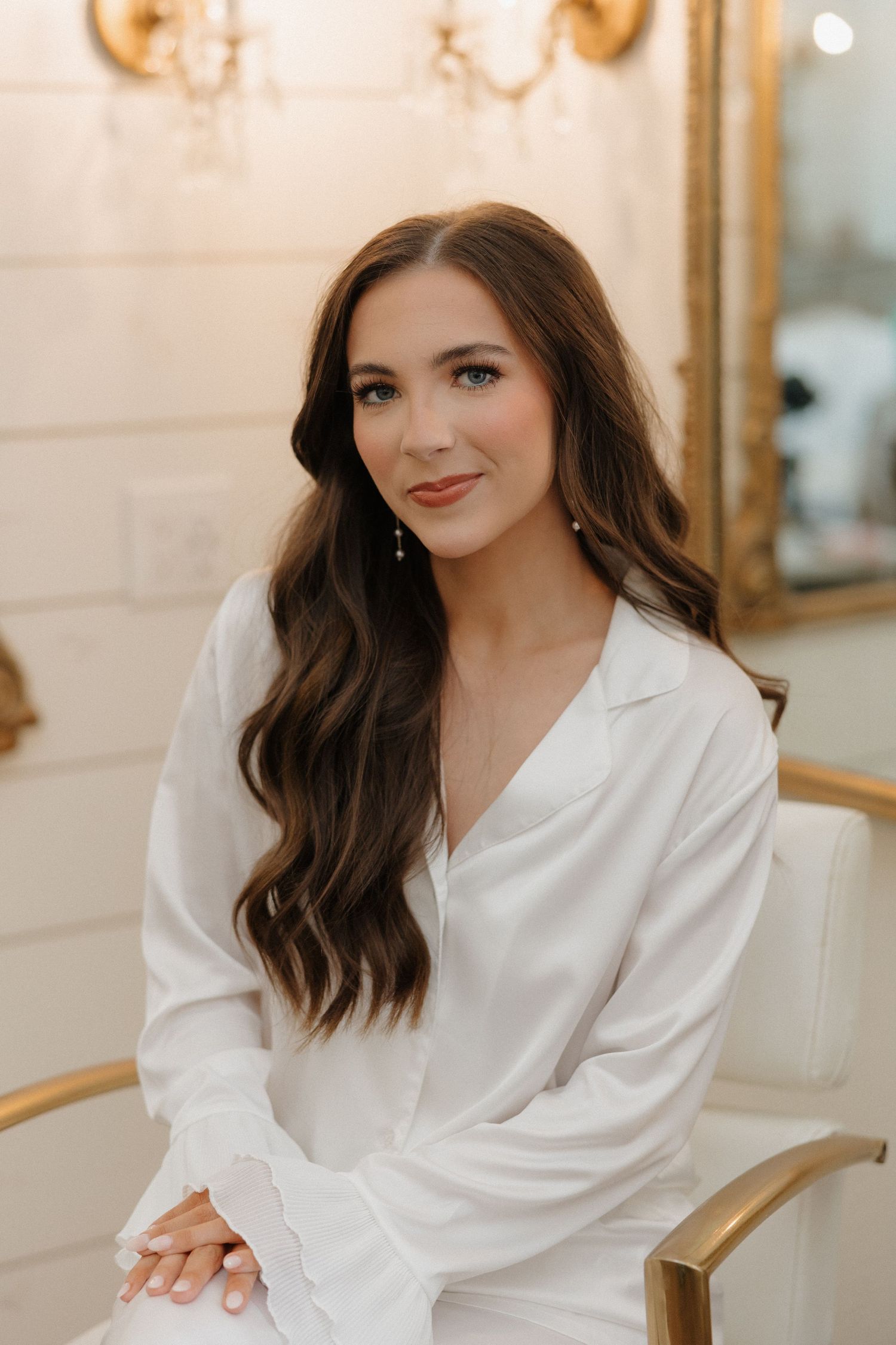Young woman in white blazer poses elegantly against light interior background in professional portrait series.