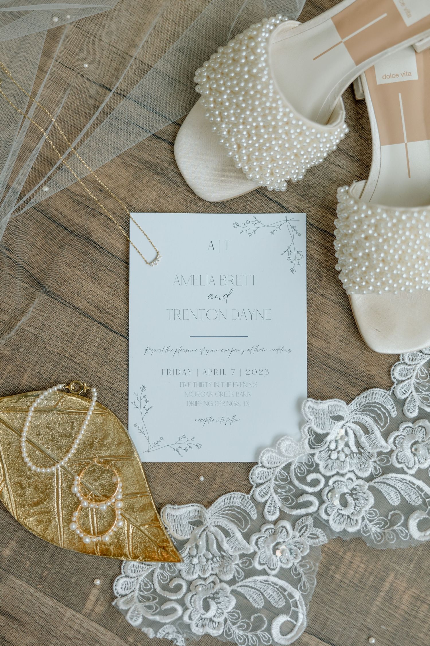Wedding accessories including lace trim, pearl necklace, and invitation cards arranged on rustic wooden surface.