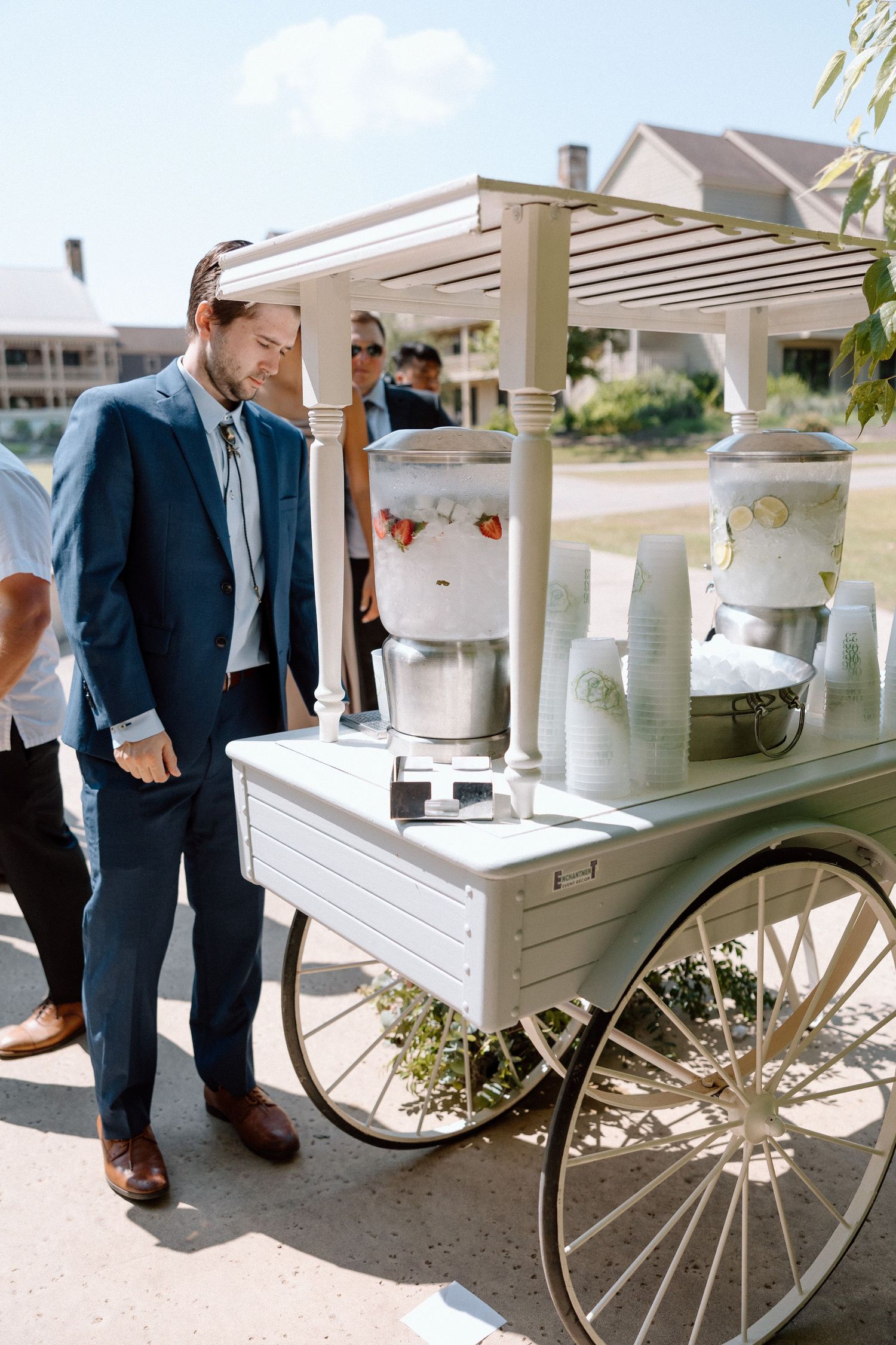 A vintage white beverage cart with wheels decorated for an elegant outdoor wedding reception.