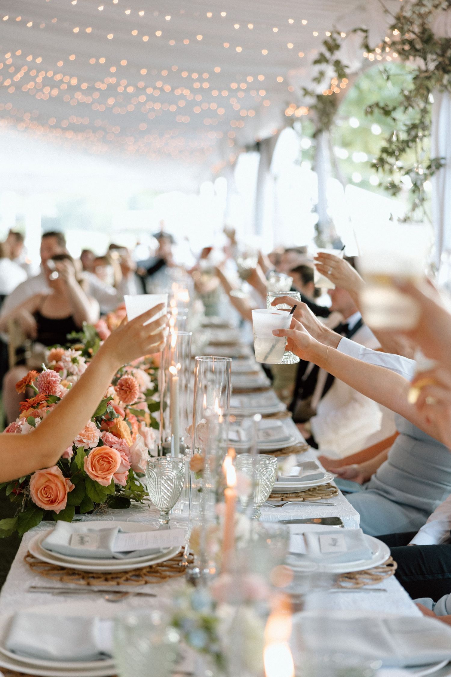 Elegant wedding reception table settings with string lights and peach floral centerpieces.