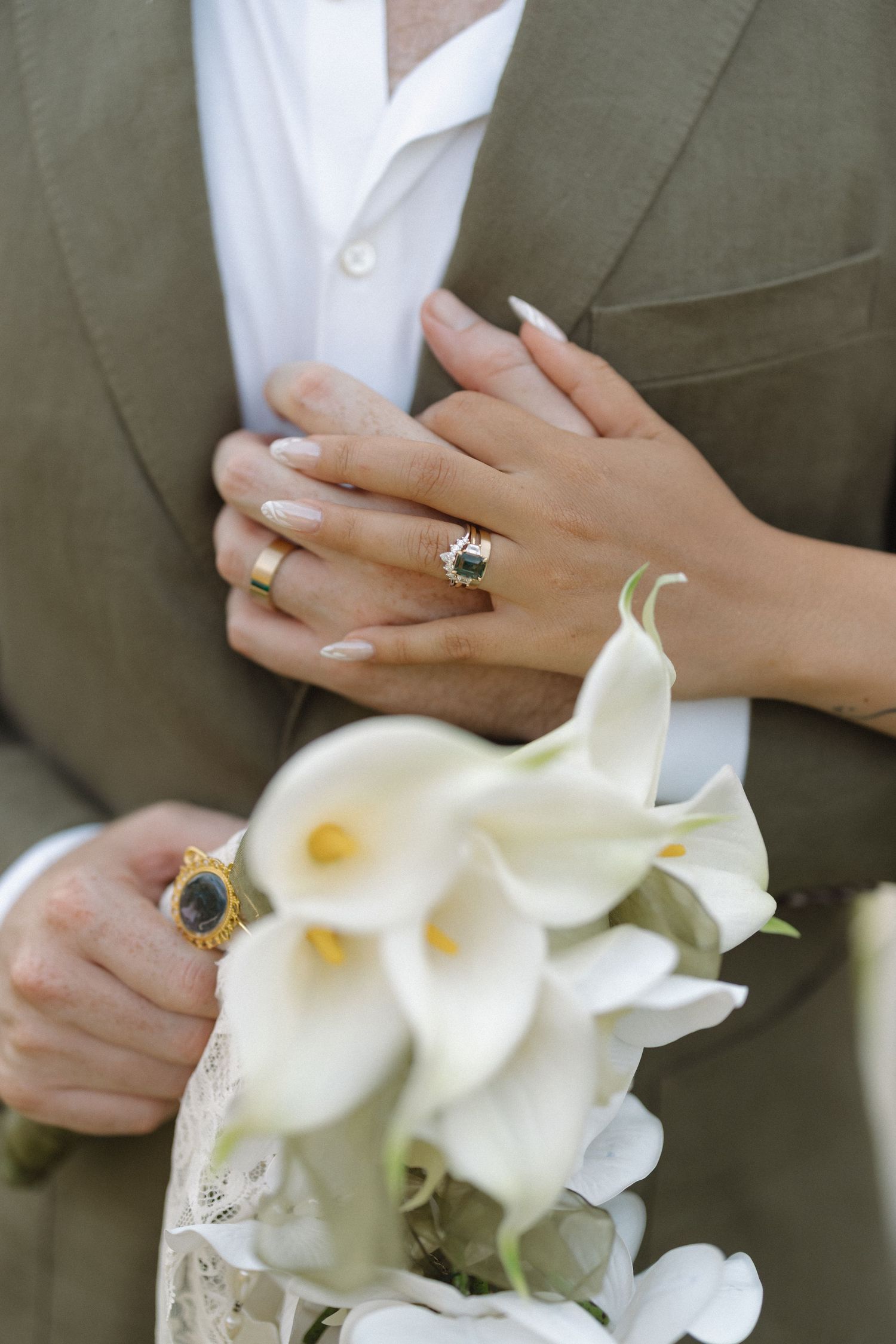 Close-up view of hands holding white calla lily bouquet with engagement ring detail.