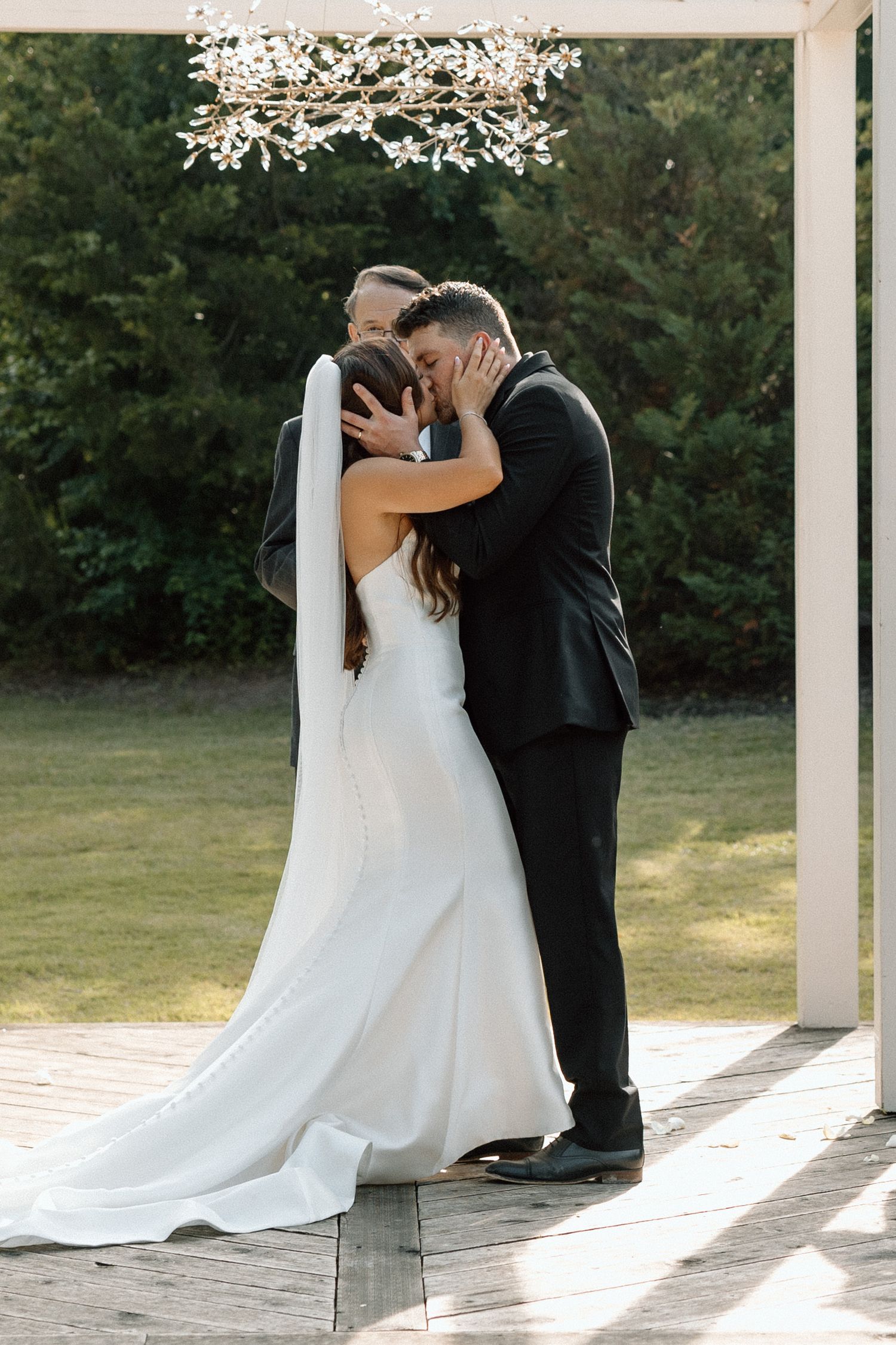 A romantic wedding couple shares an intimate moment in a sunlit outdoor pavilion with flowing white dress and veil.