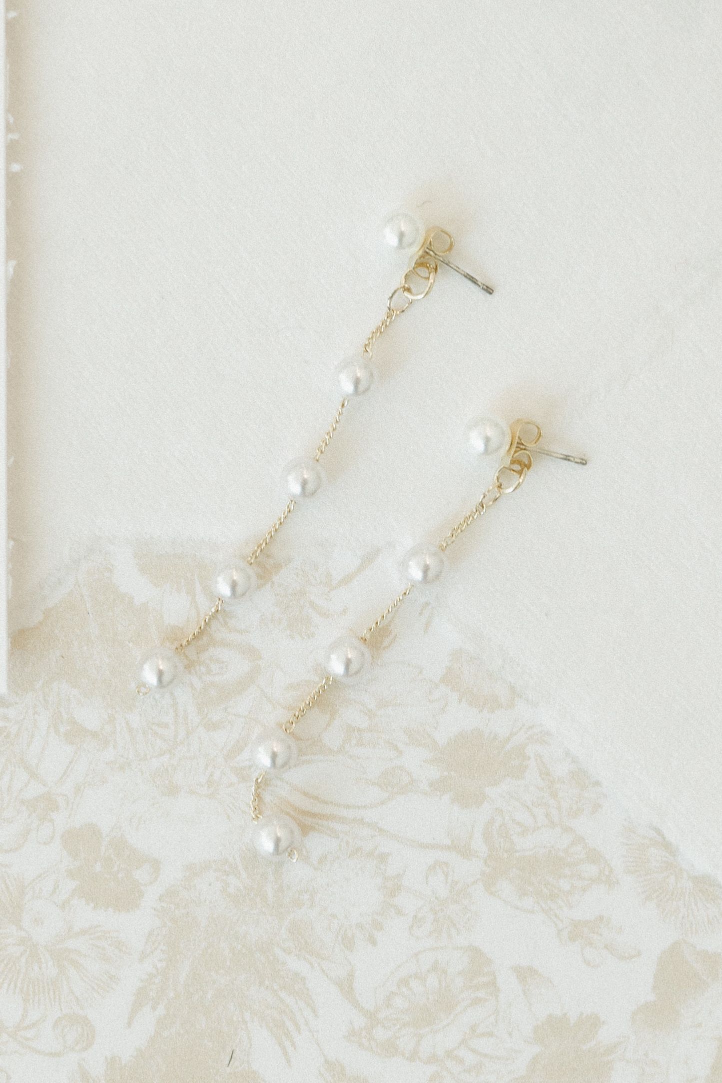 Delicate pearl and gold bridal hair accessories displayed on a light beige textured background.