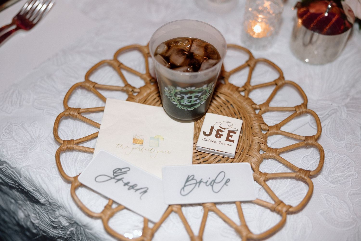 A Starbucks coffee cup and name cards arranged on a decorative woven placemat with candlelight.
