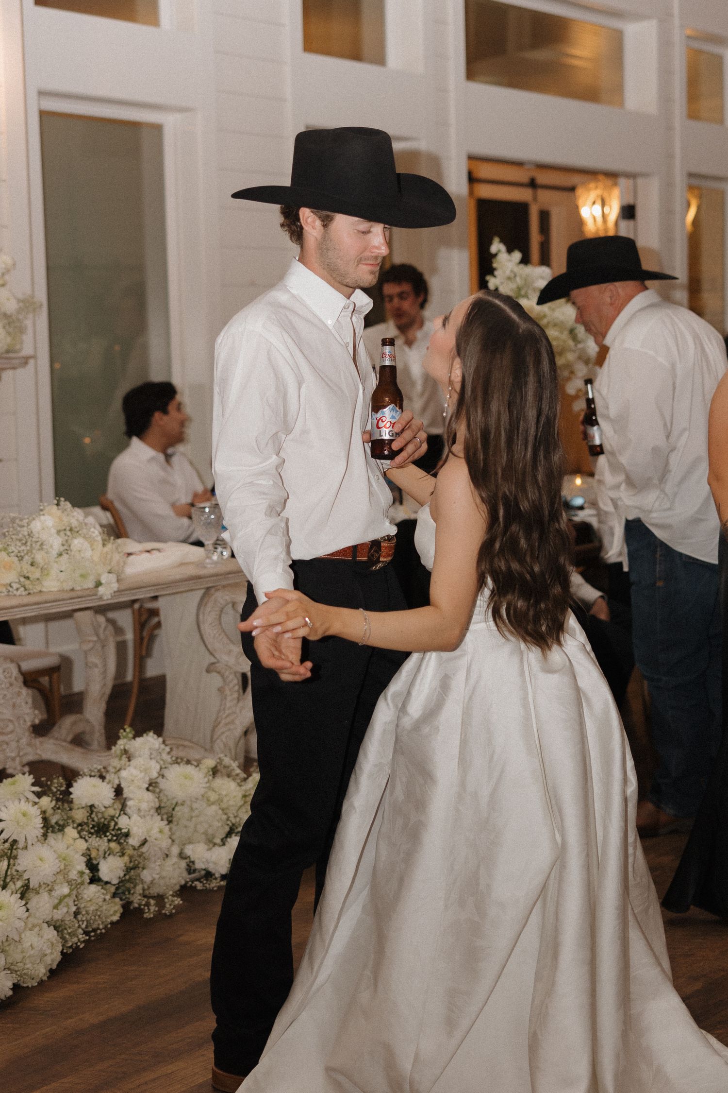Wedding couple and guests dancing together at a reception decorated with white floral arrangements.